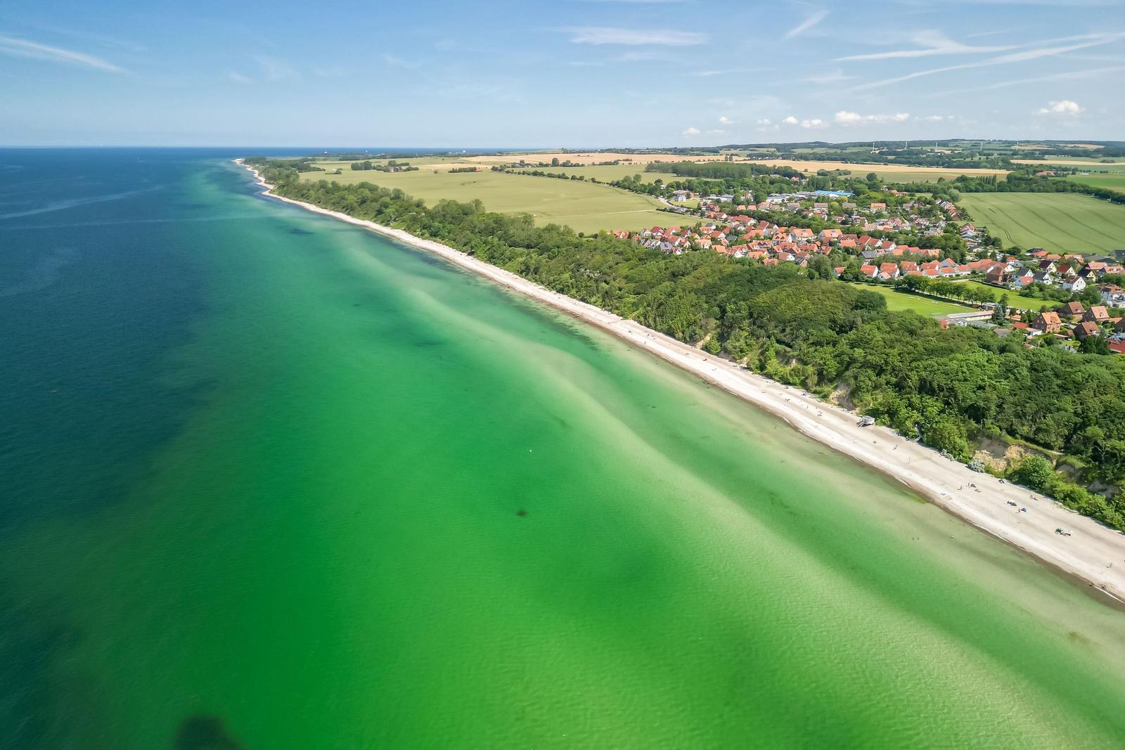 Aerial view of a beach with green water, forest, and a village.