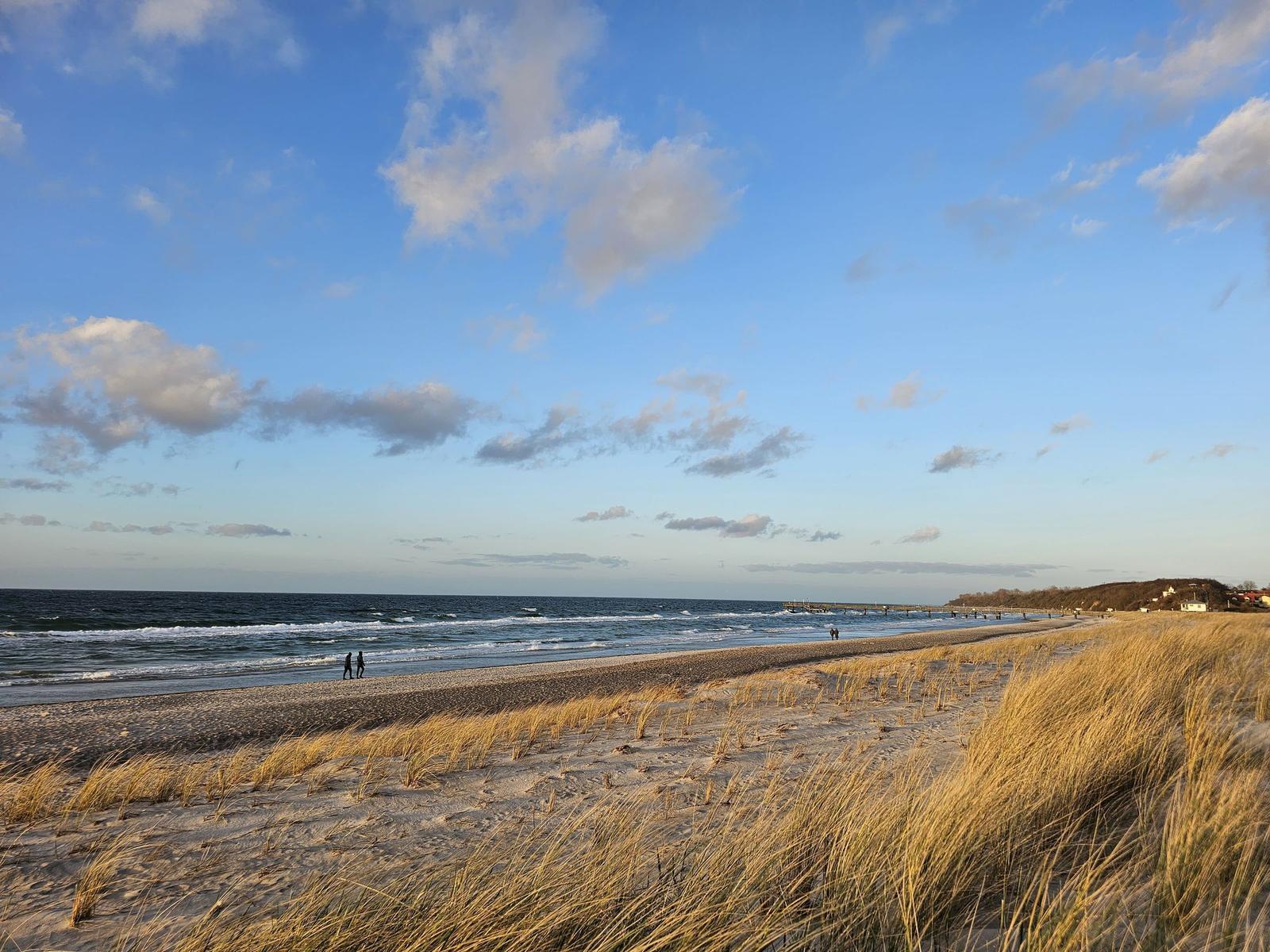Strand mit Dünen und Meer unter blauem Himmel mit Wolken.