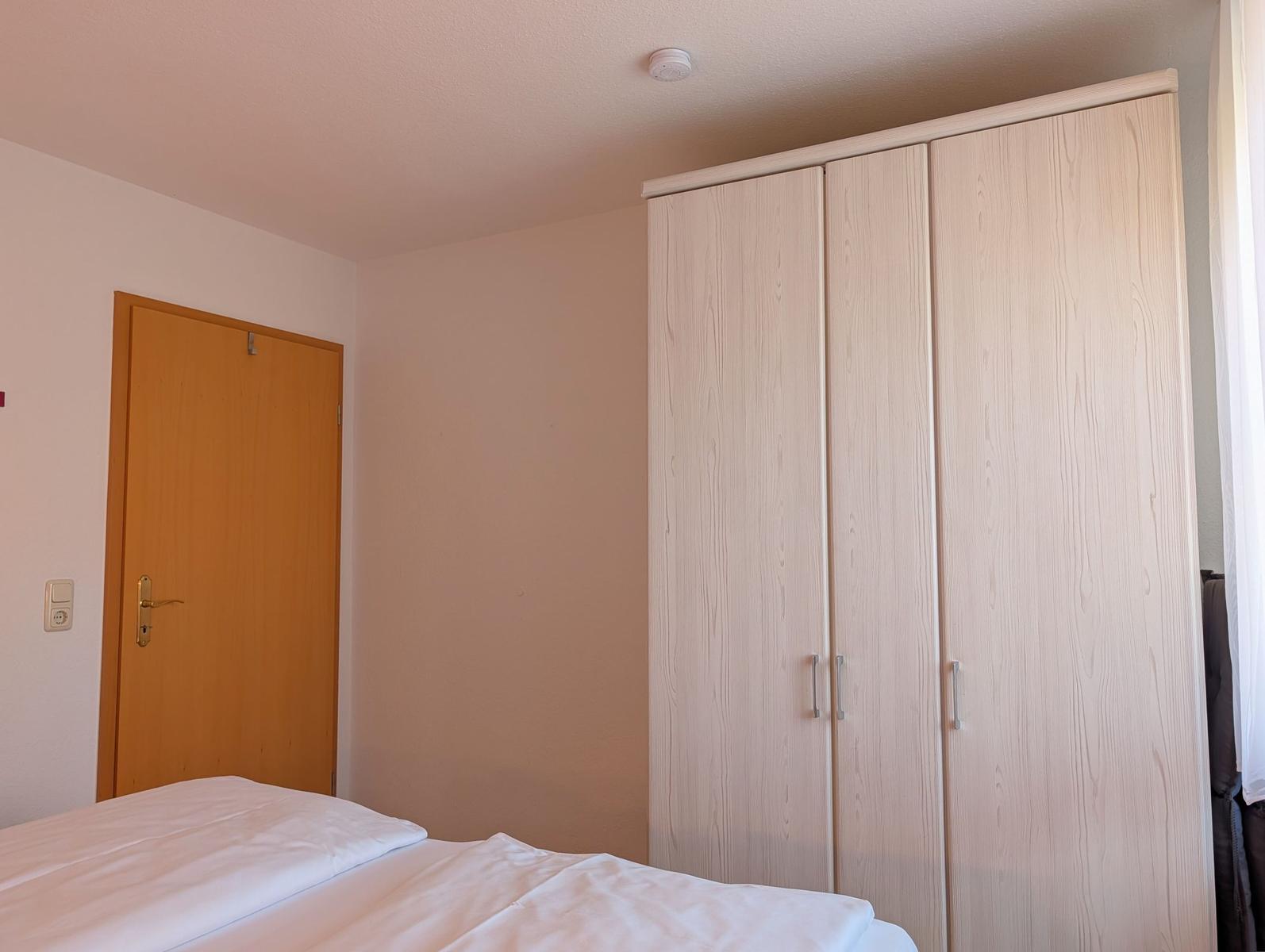 Schlafzimmer mit Bett, Kleiderschrank und Tür.
