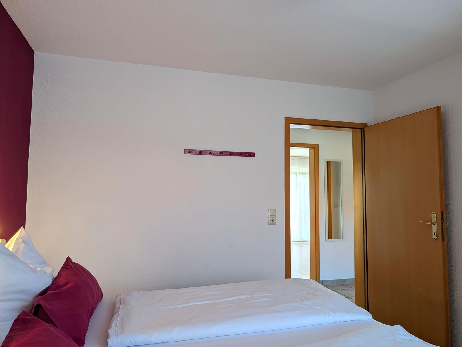 Schlafzimmer mit Bett, roter Wand und Tür zum Bad.