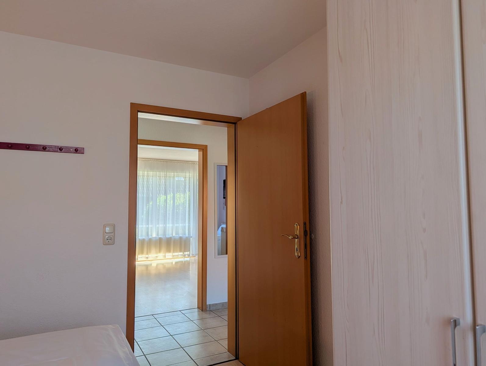 Schlafzimmer mit Tür zu Wohnbereich und Gardinen.