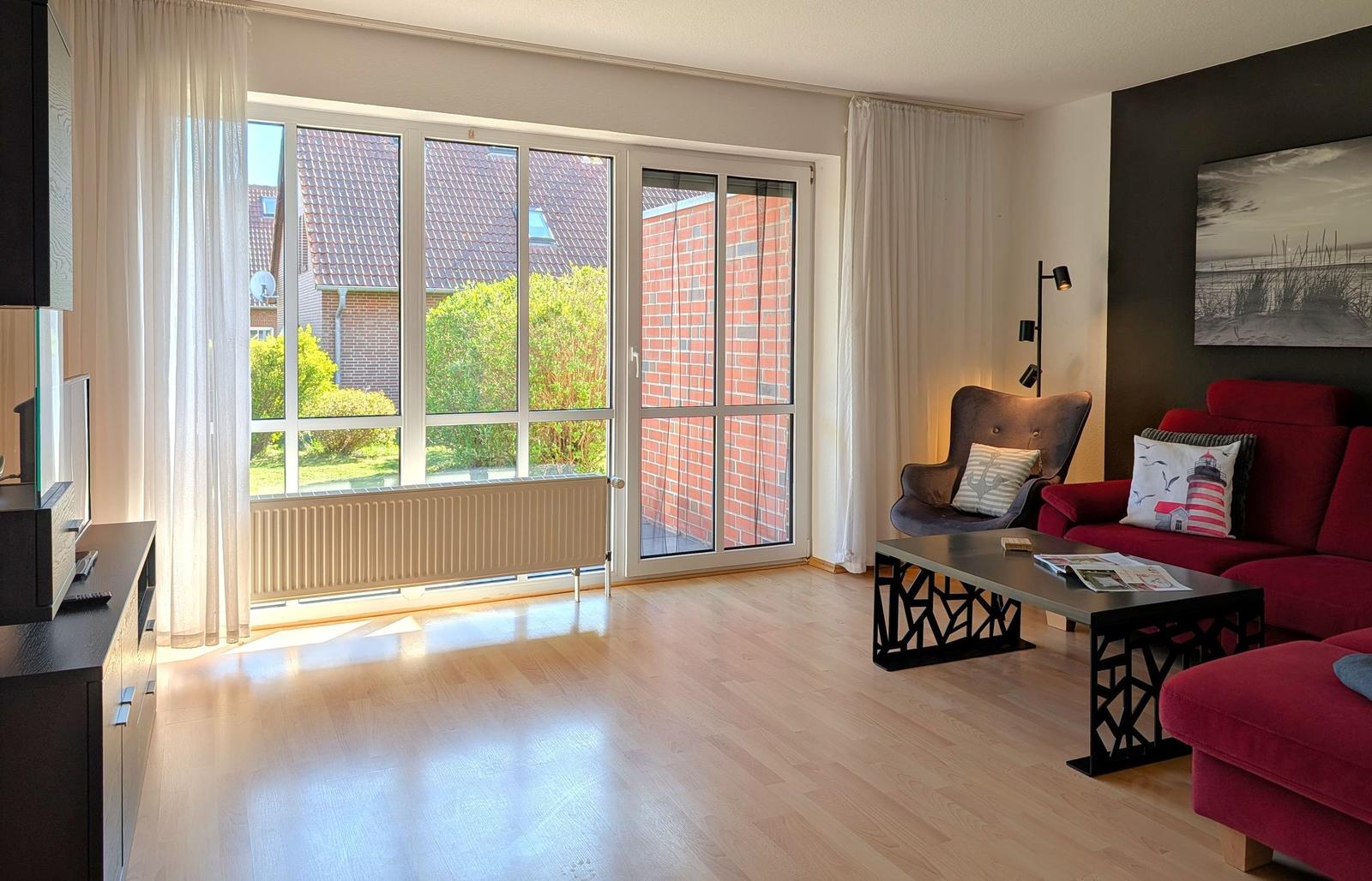 Wohnzimmer mit rotem Sofa, Glasfront und Holzboden.