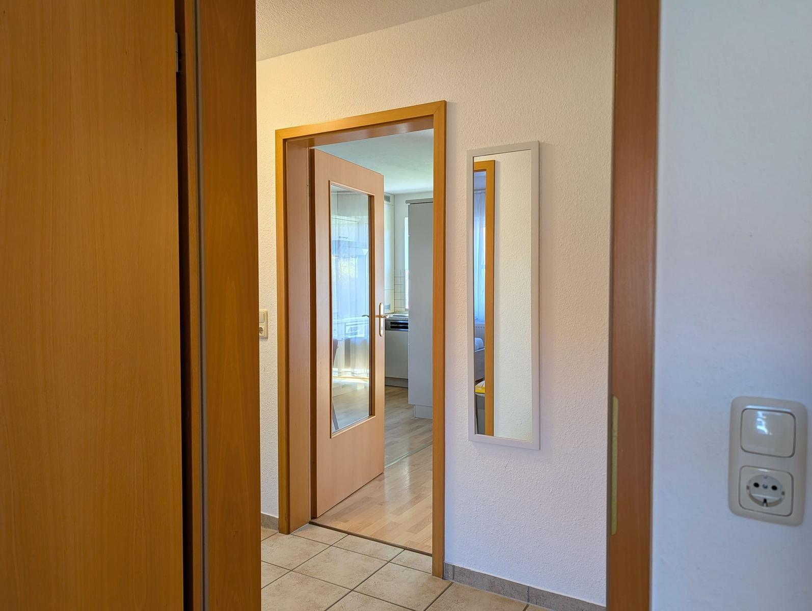 Hinter dem Schrank ist eine Tür zum Flur mit Spiegel und Lichtschalter.