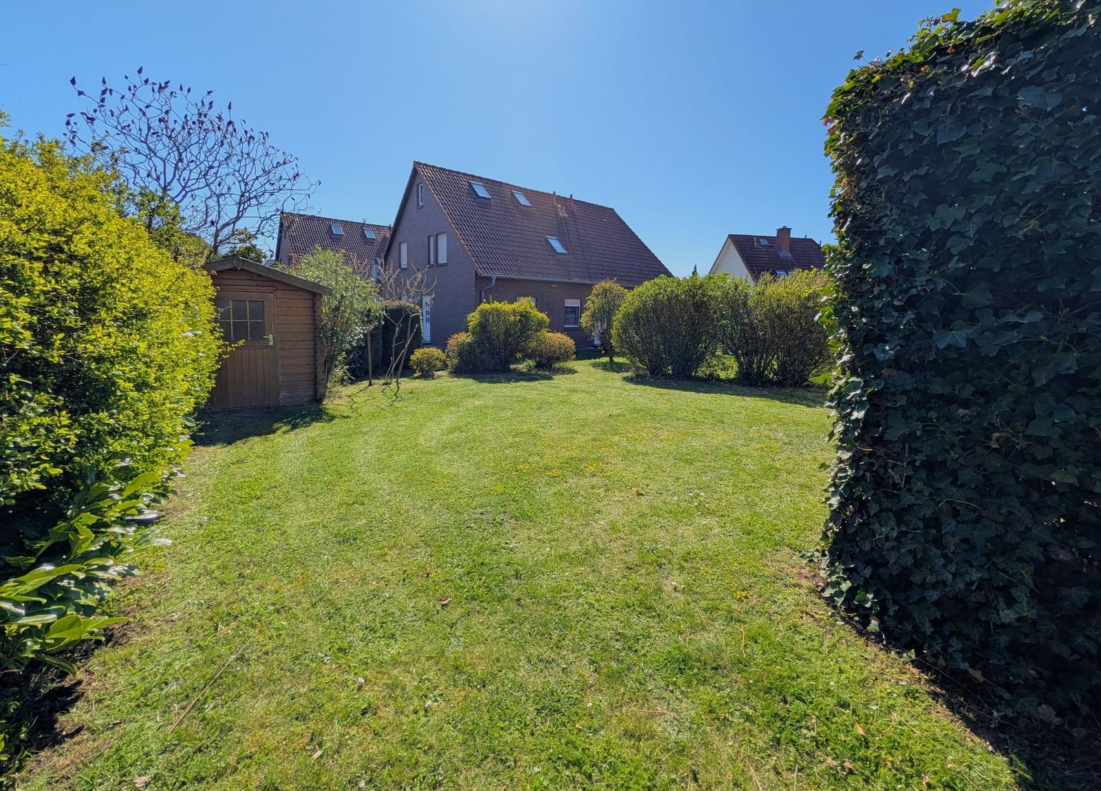 Grüner Rasenbereich mit Gartenhaus und Wohnhaus im Hintergrund.