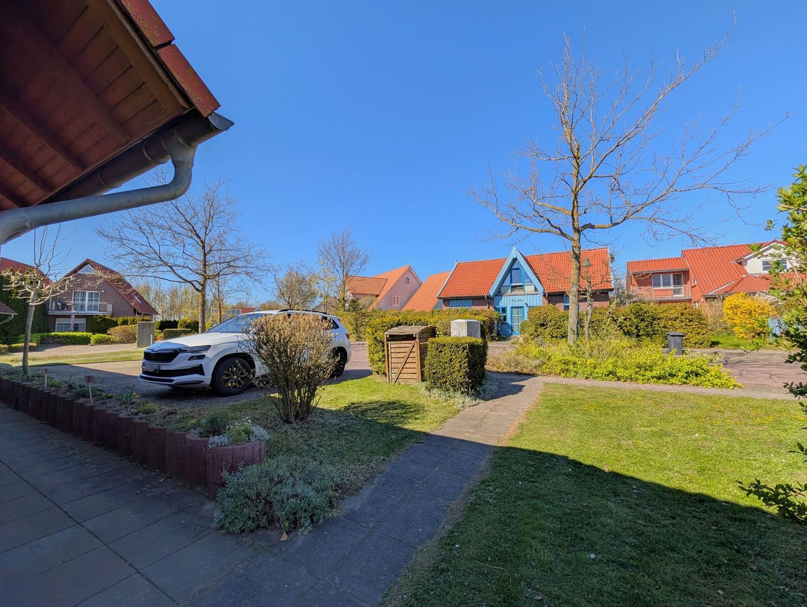 Haus mit Garten, Parkplatz und rotem Dach unter blauem Himmel.