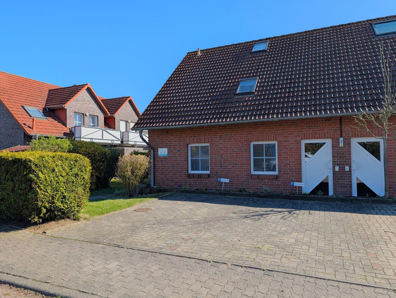 Rotes Ziegelhaus mit Dachfenstern und weißer Eingangstür. Vorgarten mit Beete und Pflasterweg.