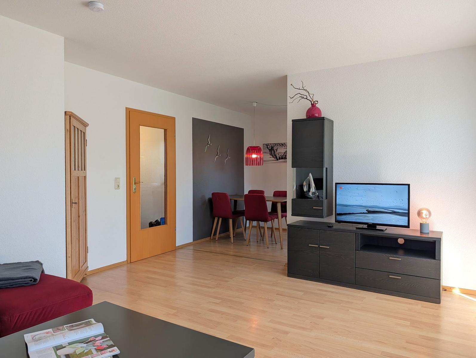 Wohn- und Essbereich mit Holzboden, TV-Schrank und roten Stühlen.