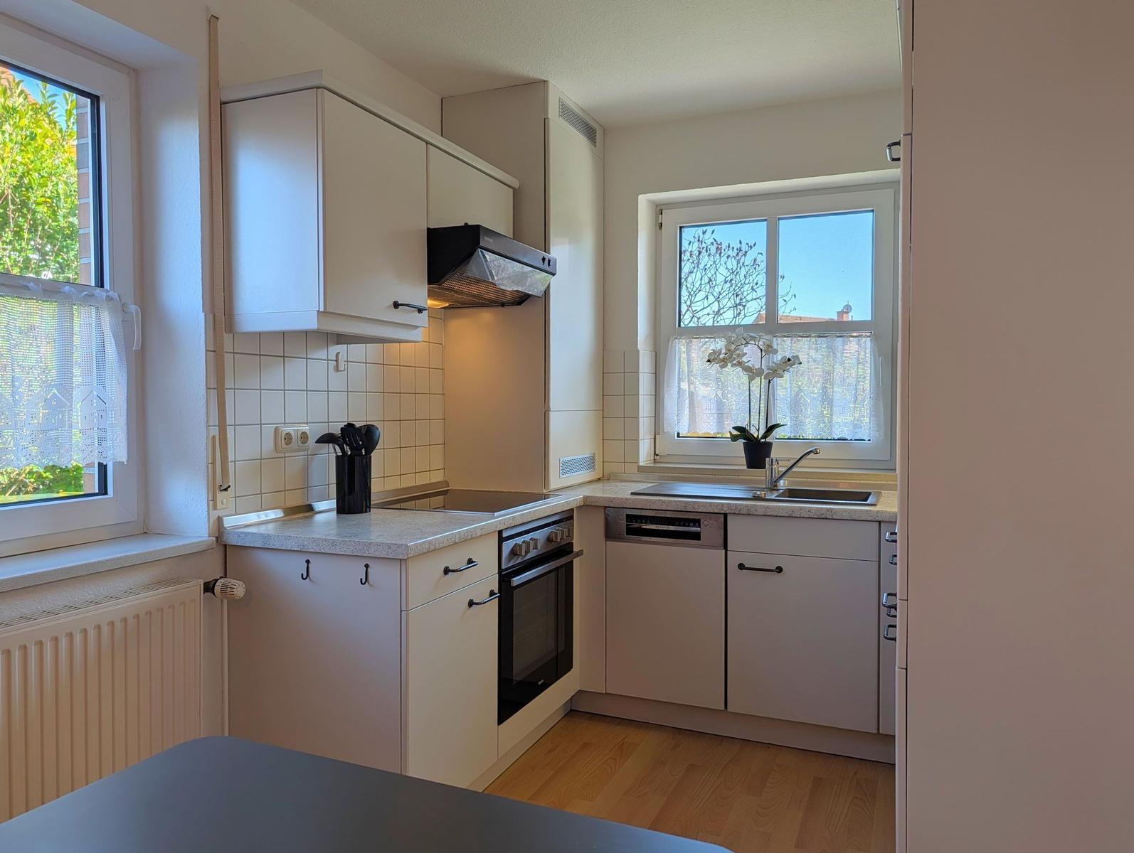 Küche mit weißen Schränken, Herd und Spüle. Fenster mit Blick auf Grün.