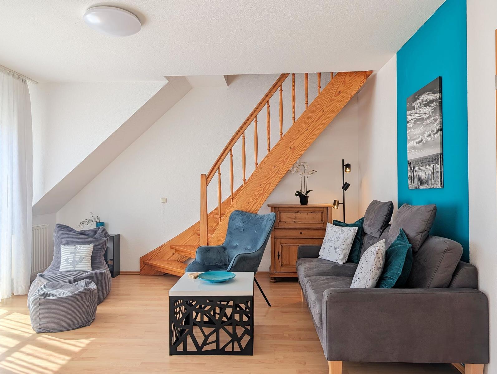 Living room with sofa, armchair, and wooden staircase. Blue wall and wooden floor.