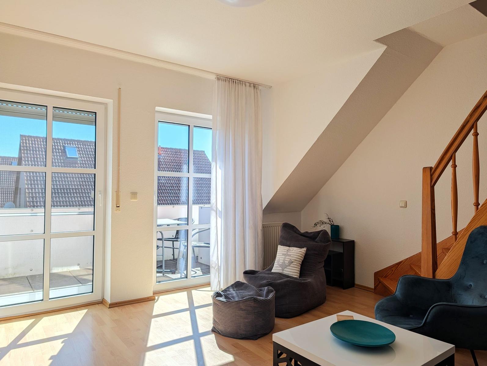 Living room with seating, glass doors, and wooden floor. Staircase on the right.