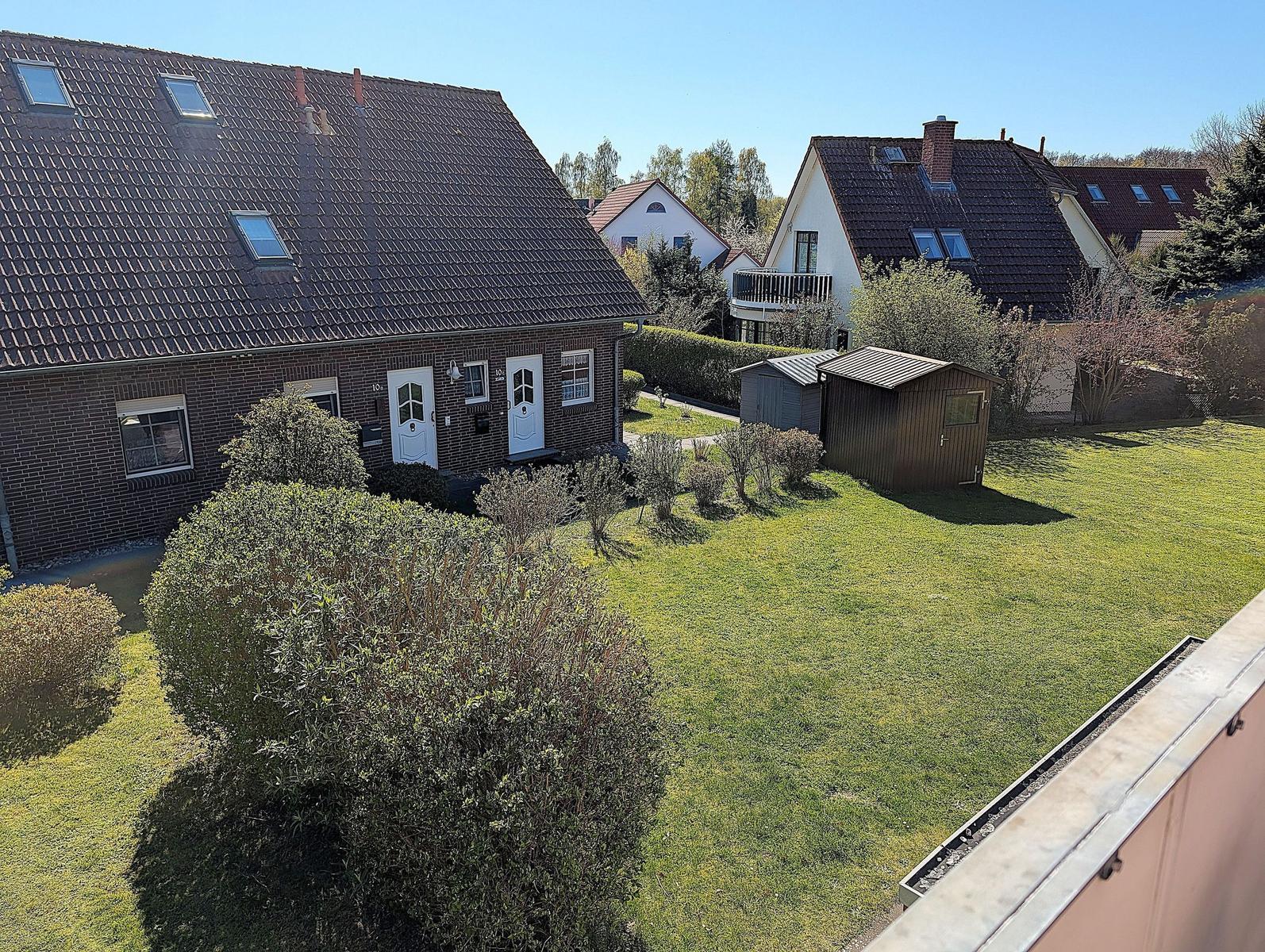 House with garden, terrace, and small sheds in the background.