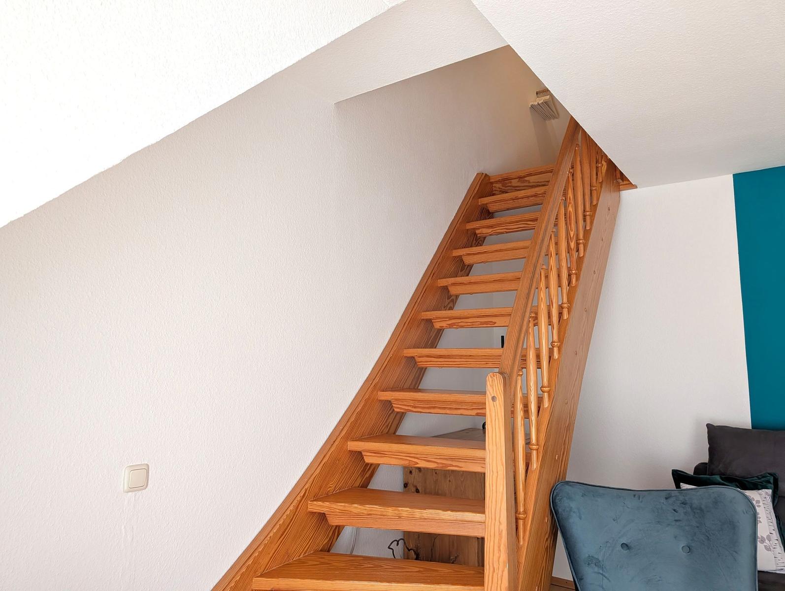 Wooden stairs with handrail lead to upper level. Wall color white and turquoise.