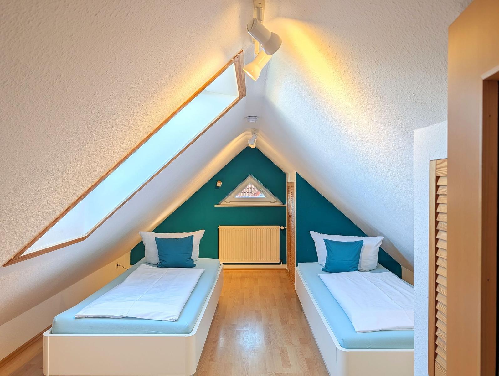 Two single beds under sloped ceilings with wooden floor and skylight.