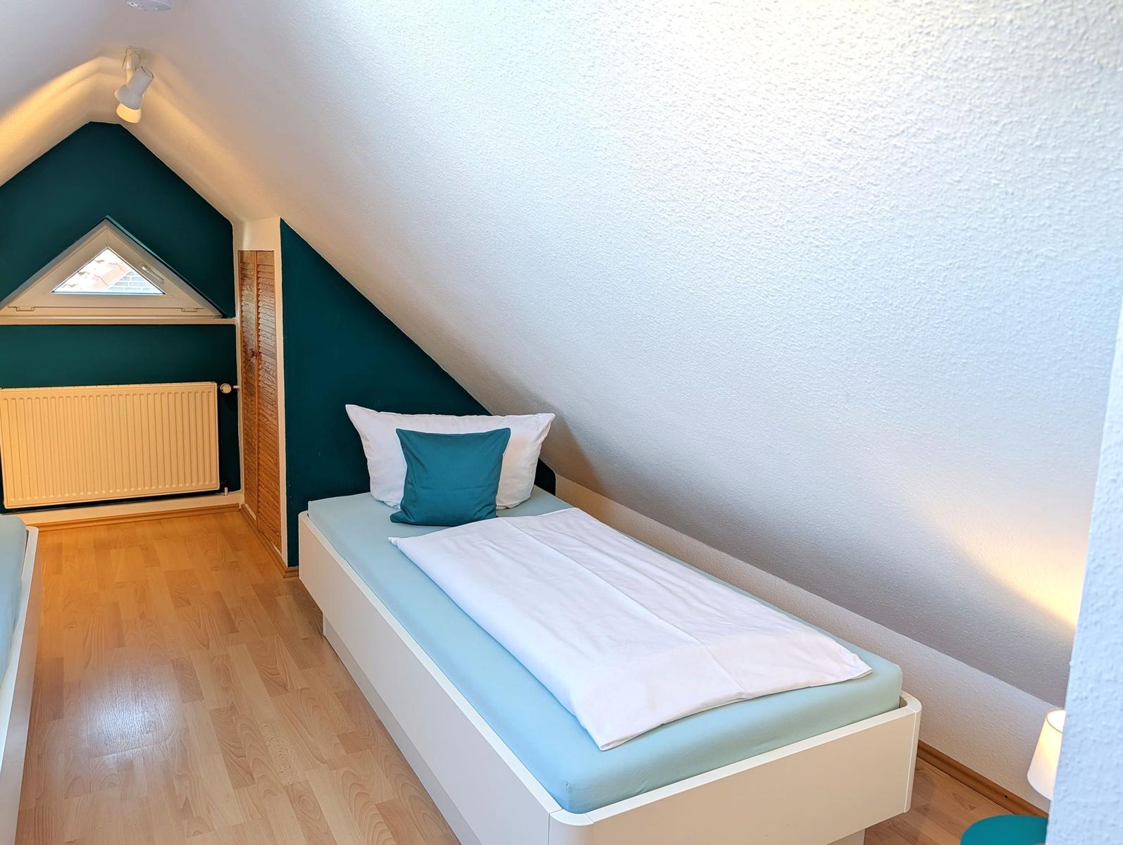 Bedroom with sloped ceiling, bed with pillows, and wooden floor.