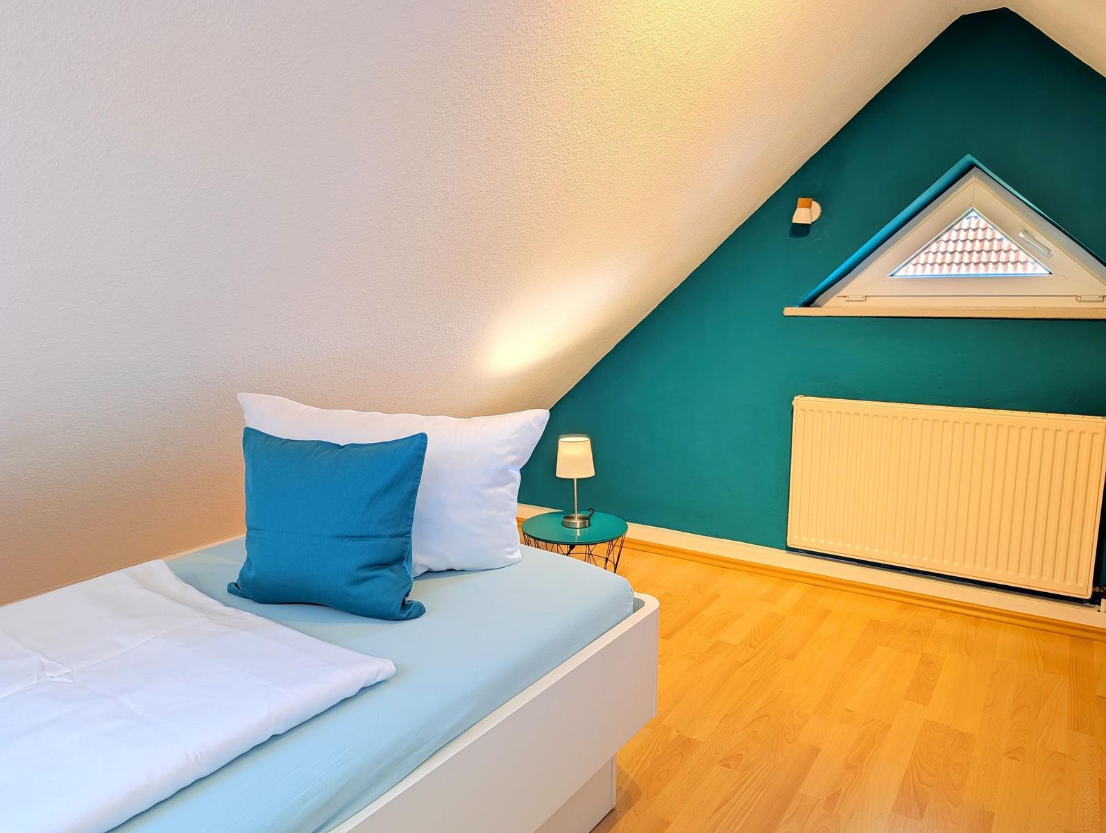 Bedroom with sloped ceiling, bed, nightstand, and radiator.