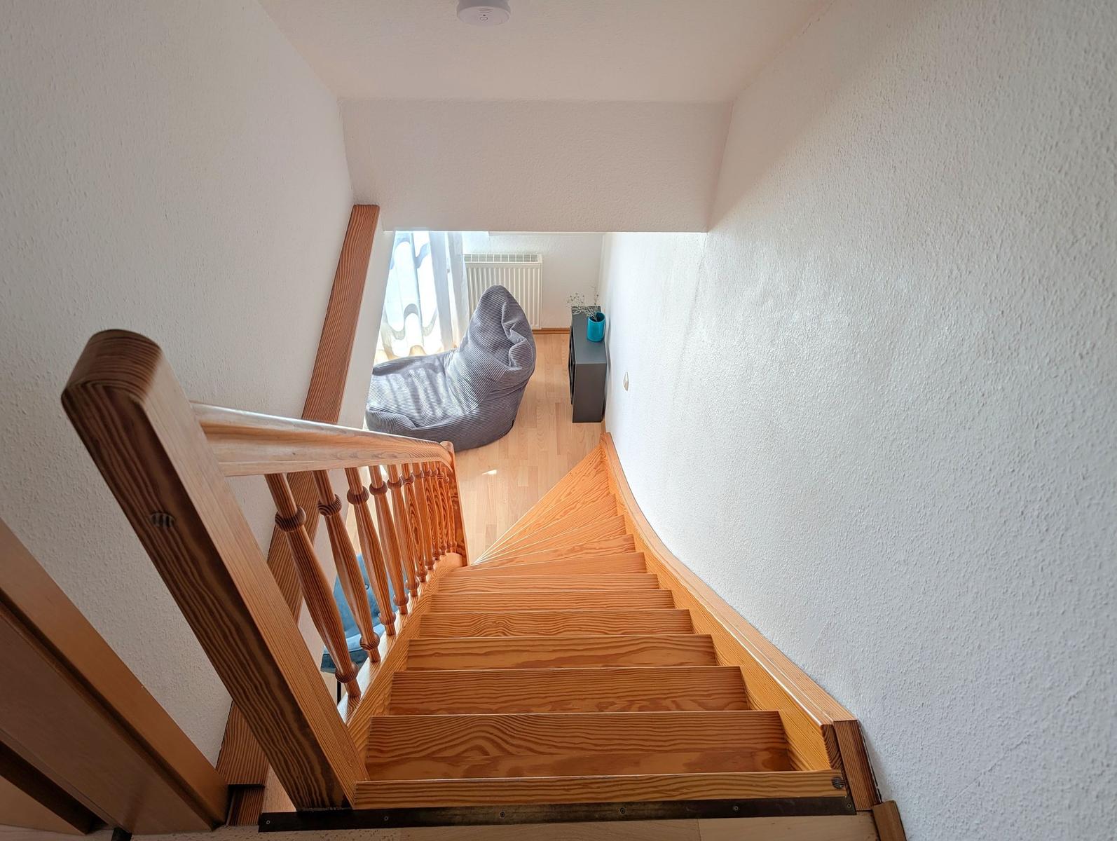 Wooden staircase leads to a room with a bean bag chair and window.