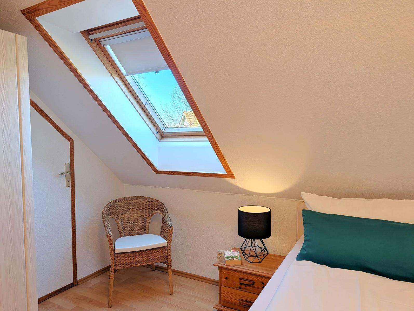 Bedroom with sloped ceiling, skylight, chair, and nightstand.