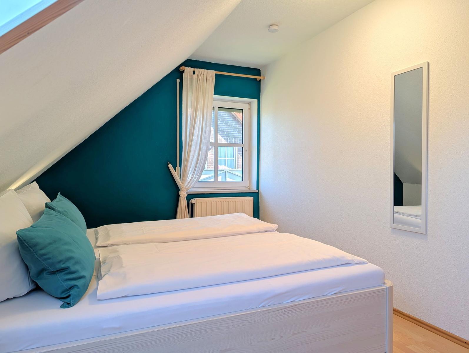 Bedroom with sloped ceiling, bed, window, and mirror on the wall.