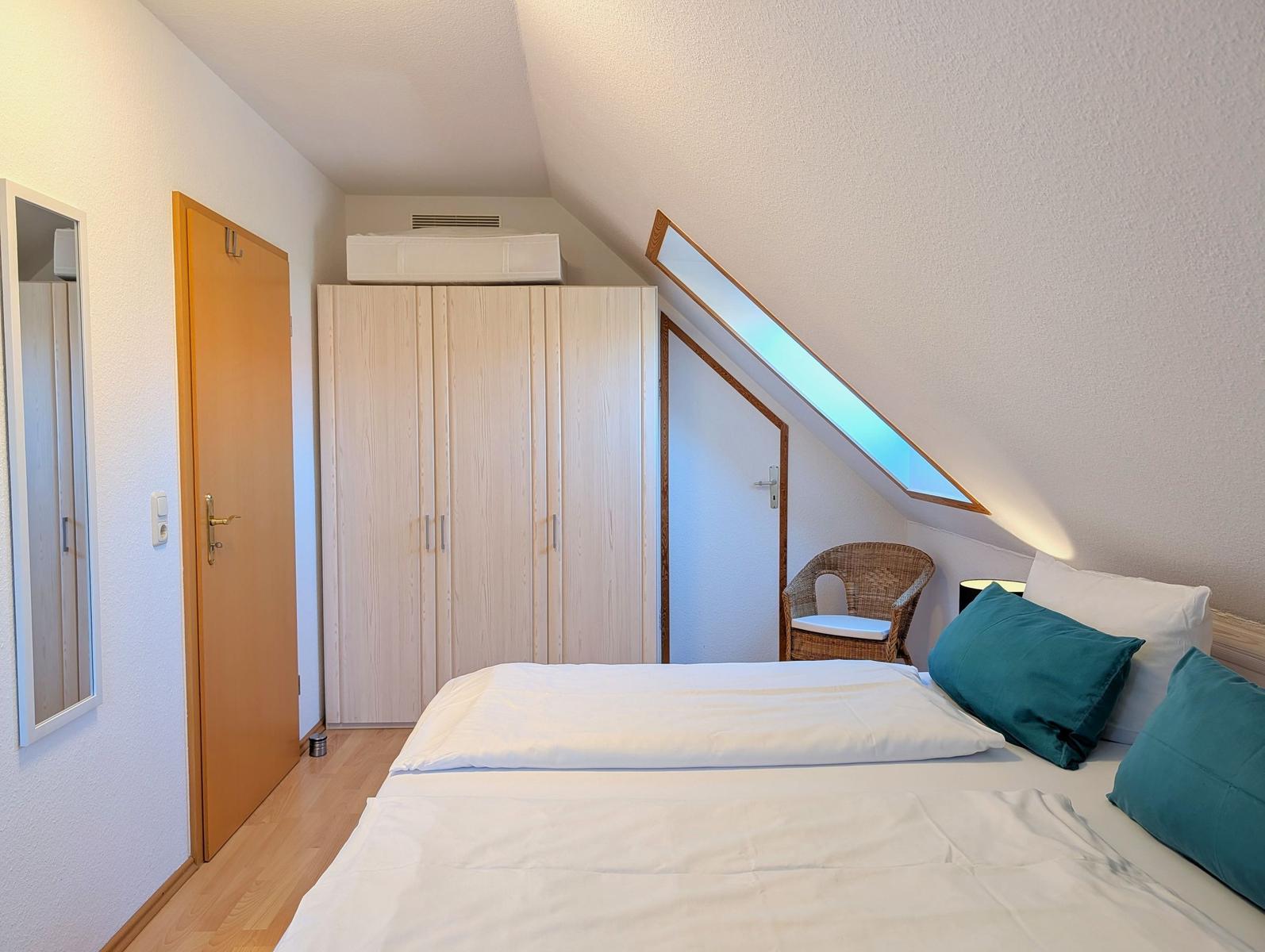 Bedroom with sloped ceiling, bed, wardrobe, and seating area.