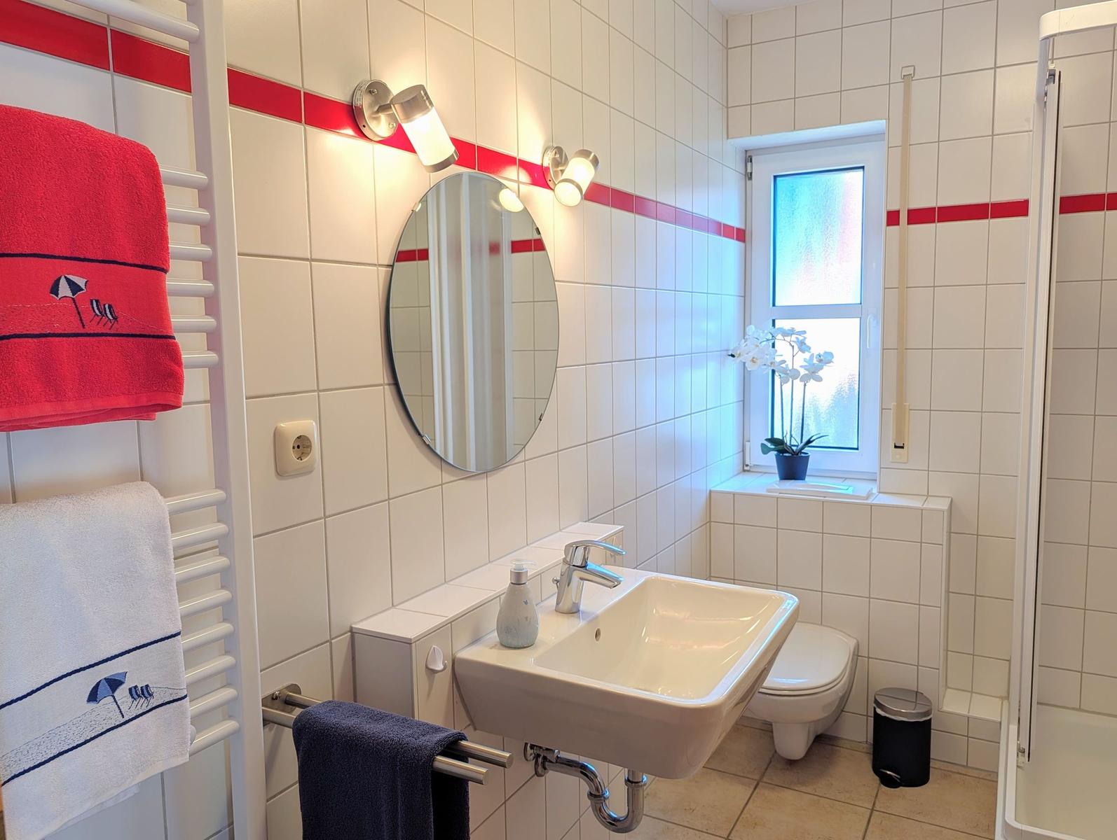 Bathroom with sink, toilet, and shower. White tiles with red stripe.