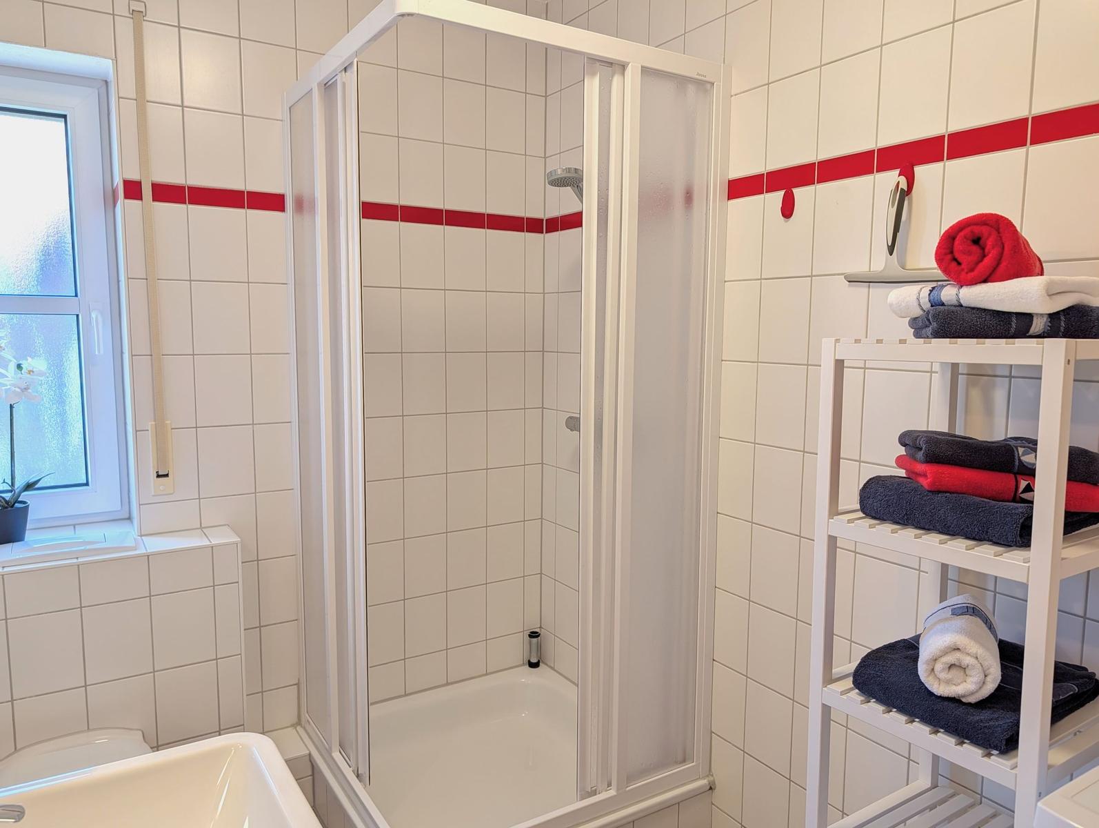 Bathroom with shower, window, and towel rack with towels.