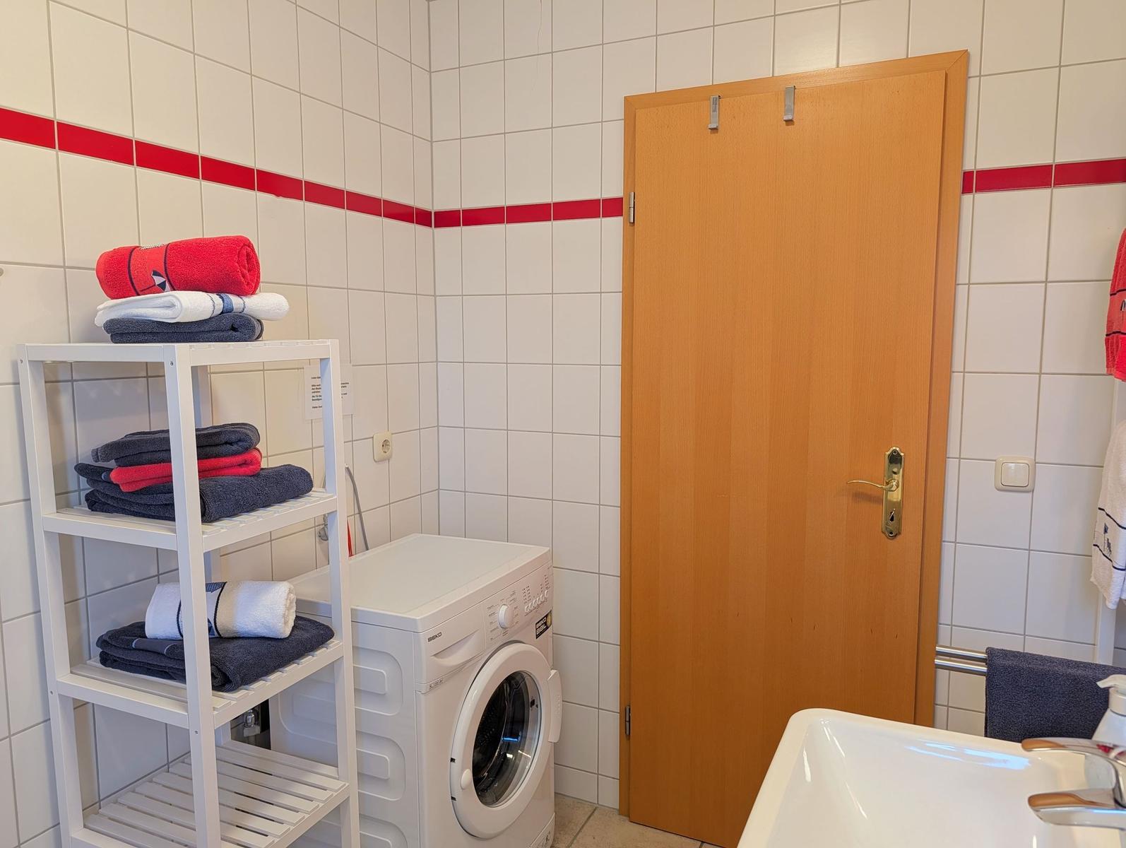Washing machine, towel rack, and sink in bathroom with white tiles and red stripe.