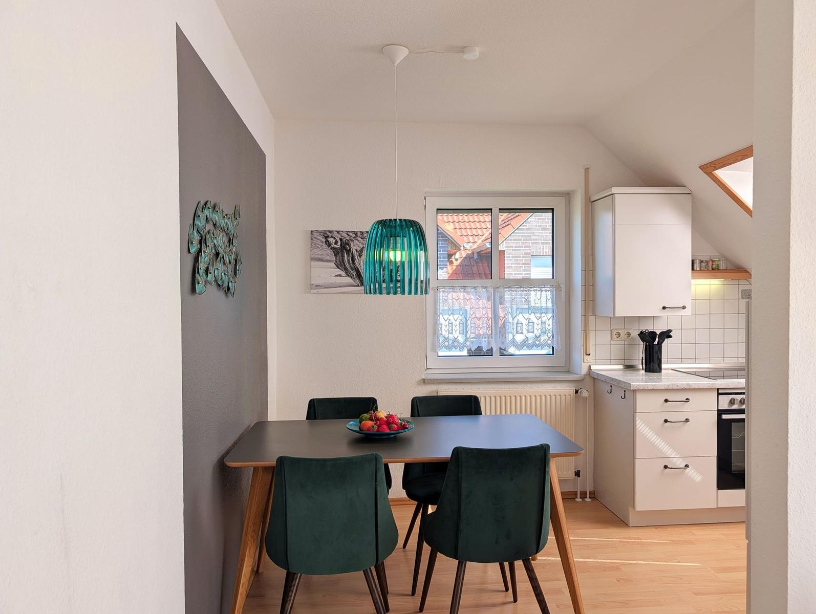 Dining area with table, chairs, and window. Kitchen with countertop and cabinets.