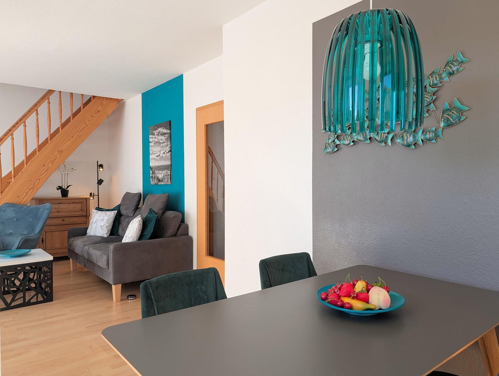 Dining area with table and chairs, wall decor, and view into living room with sofa and staircase.