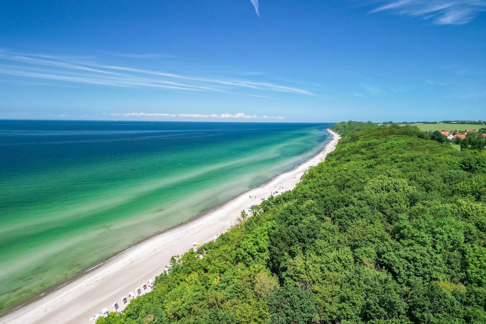 Beach with sandy shore and green coastline under blue sky.