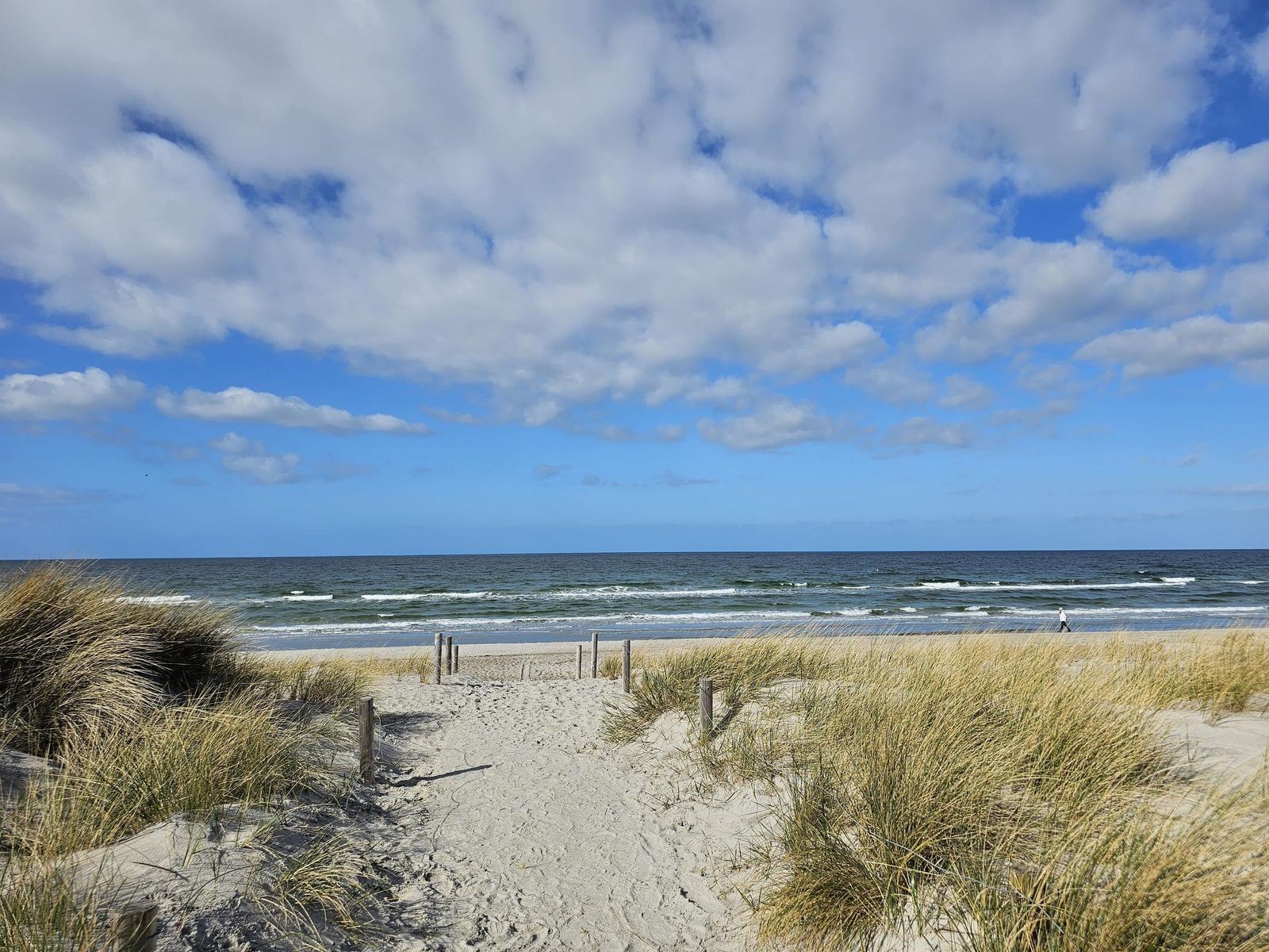 Sandy path leads through dunes to the Baltic Sea. Blue sky with white clouds.