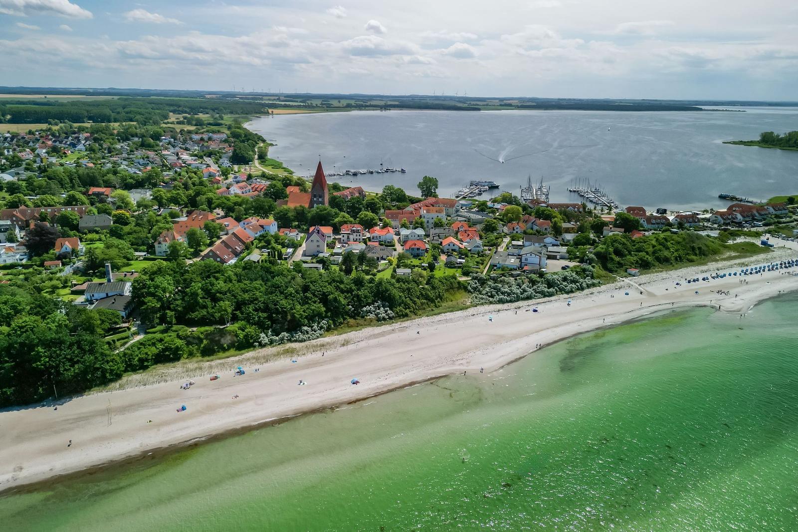 Aerial view of coastal village with beach, harbor, and red-roofed houses near water.
