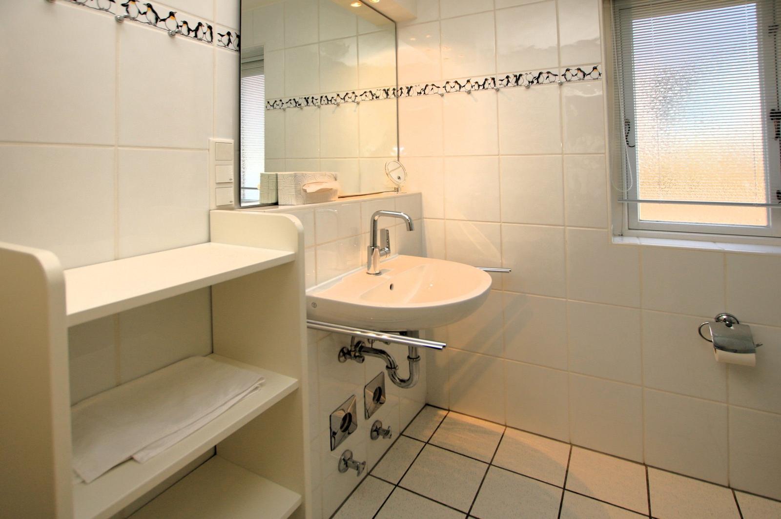 Badezimmer mit Waschbecken, Spiegel und Fenster. Wandfliesen mit Pinguinmotiv.