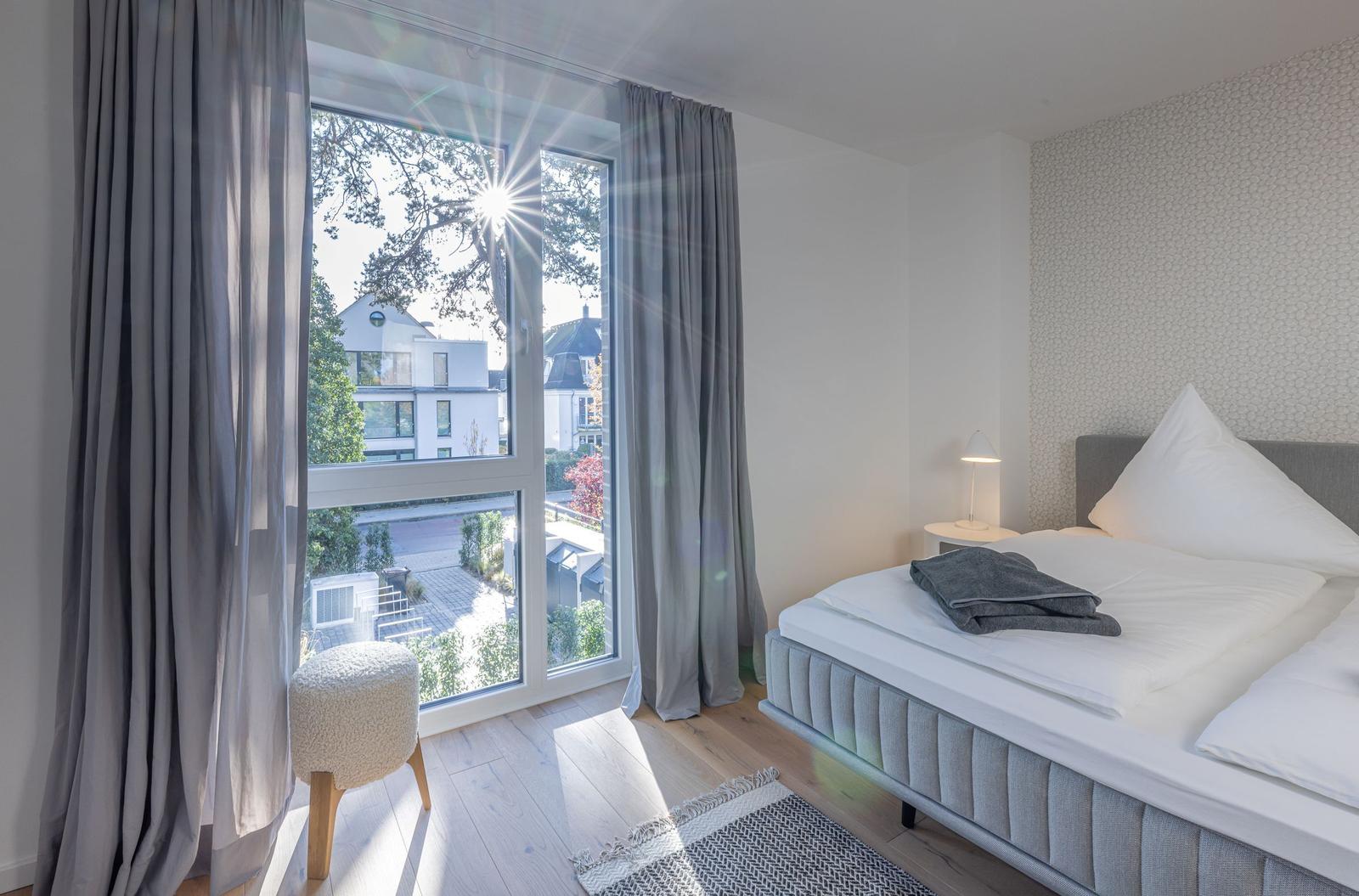 Schlafzimmer mit Blick auf Außenbereich. Bett, Nachttisch und Fenster mit Vorhängen.