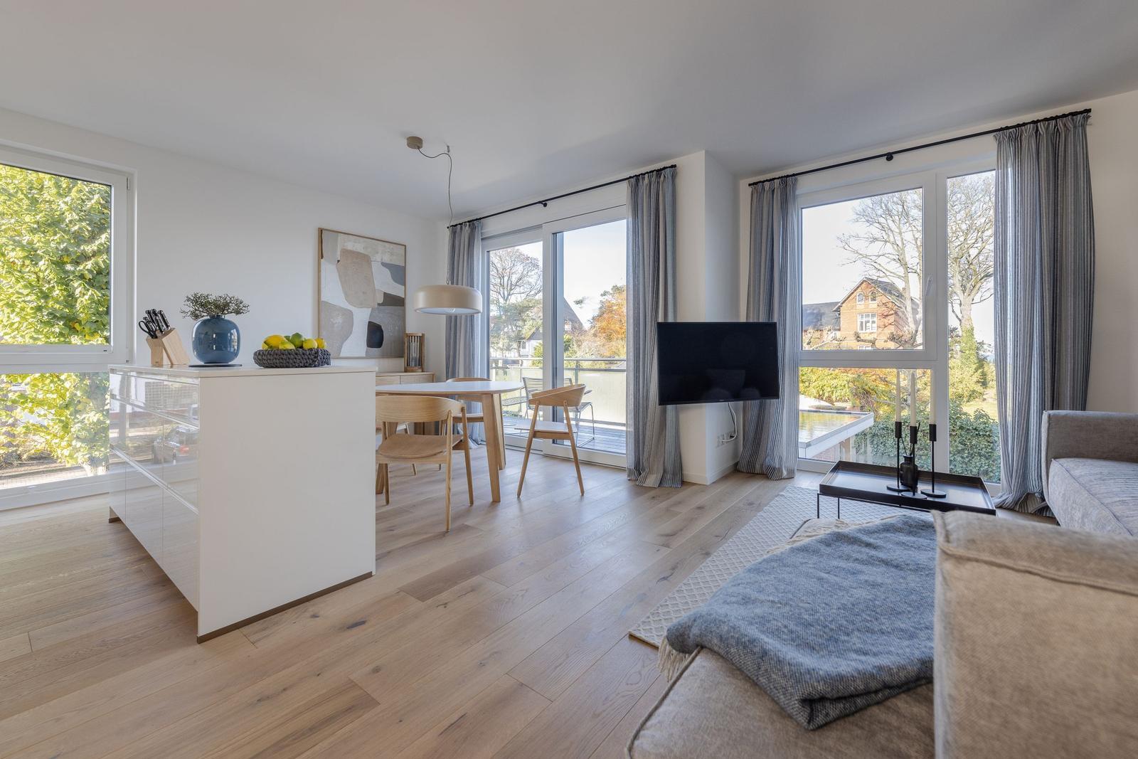 Wohn- und Essbereich mit Holzboden, großen Fenstern und einem Balkon.