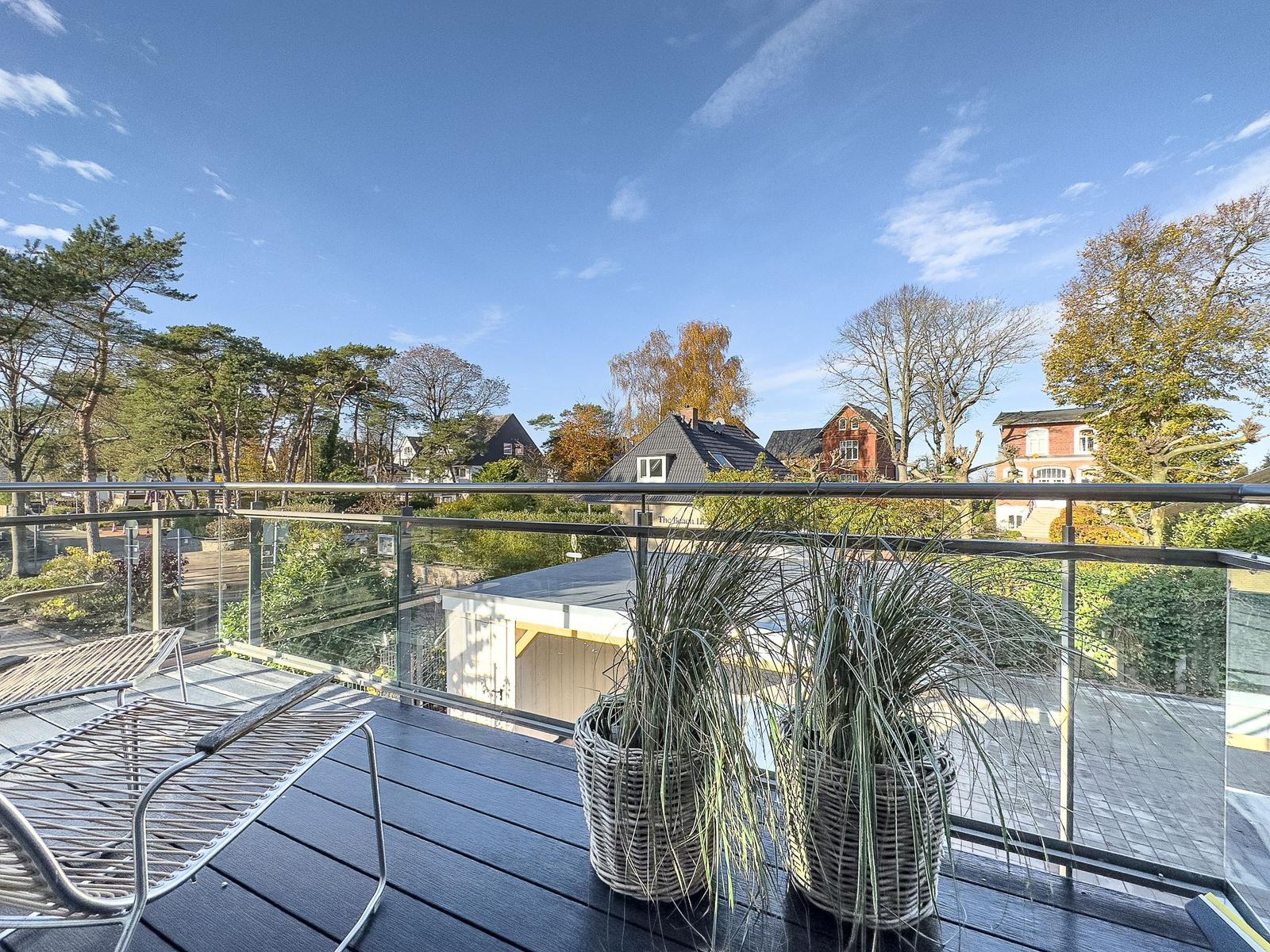 Terrasse mit Loungemöbeln und Pflanzen. Blick auf Wohnhäuser und Bäume unter blauem Himmel.