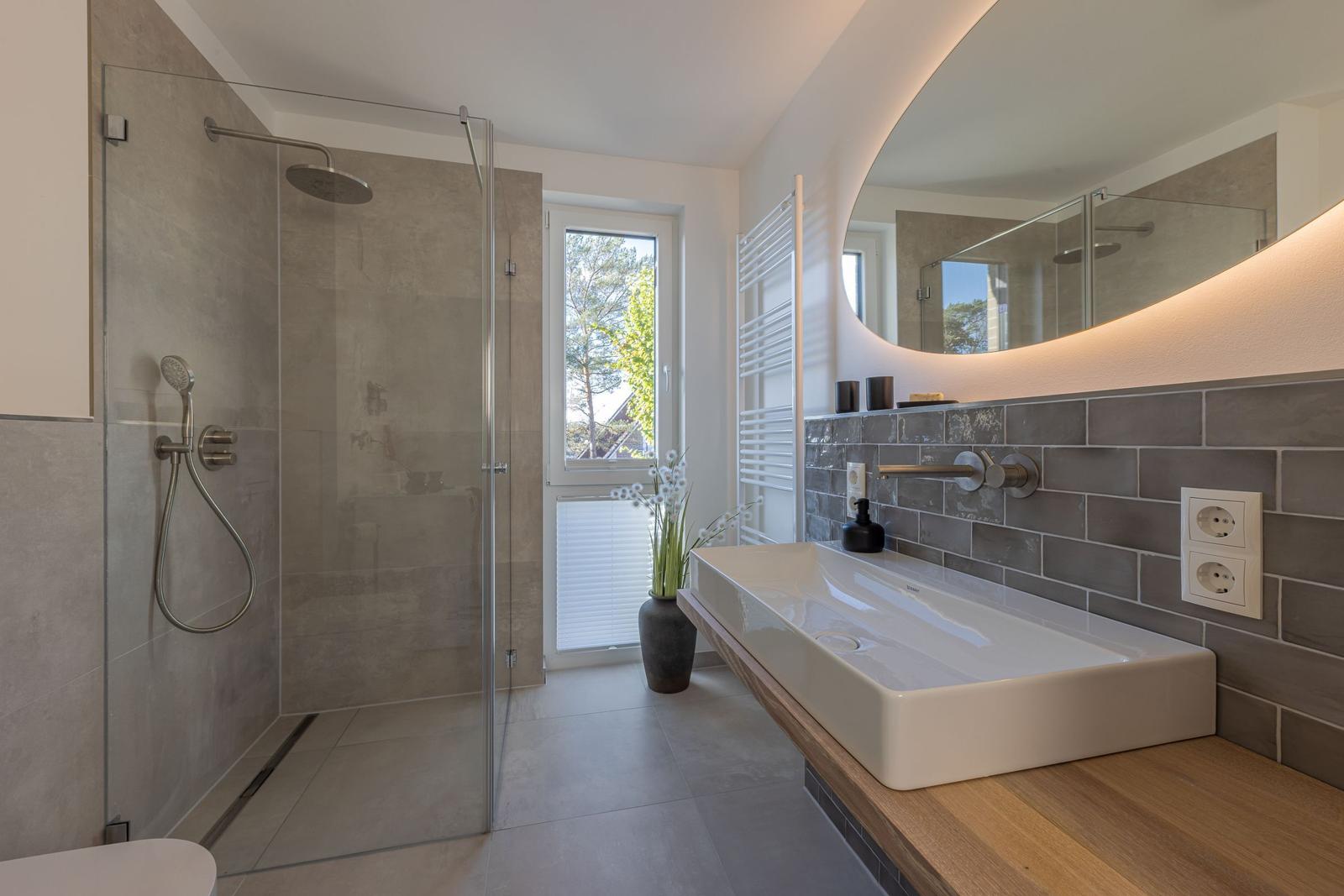 Moderne Dusche mit Glaswand, Waschbecken auf Holzunterlage und Fenster mit Blick nach draußen.