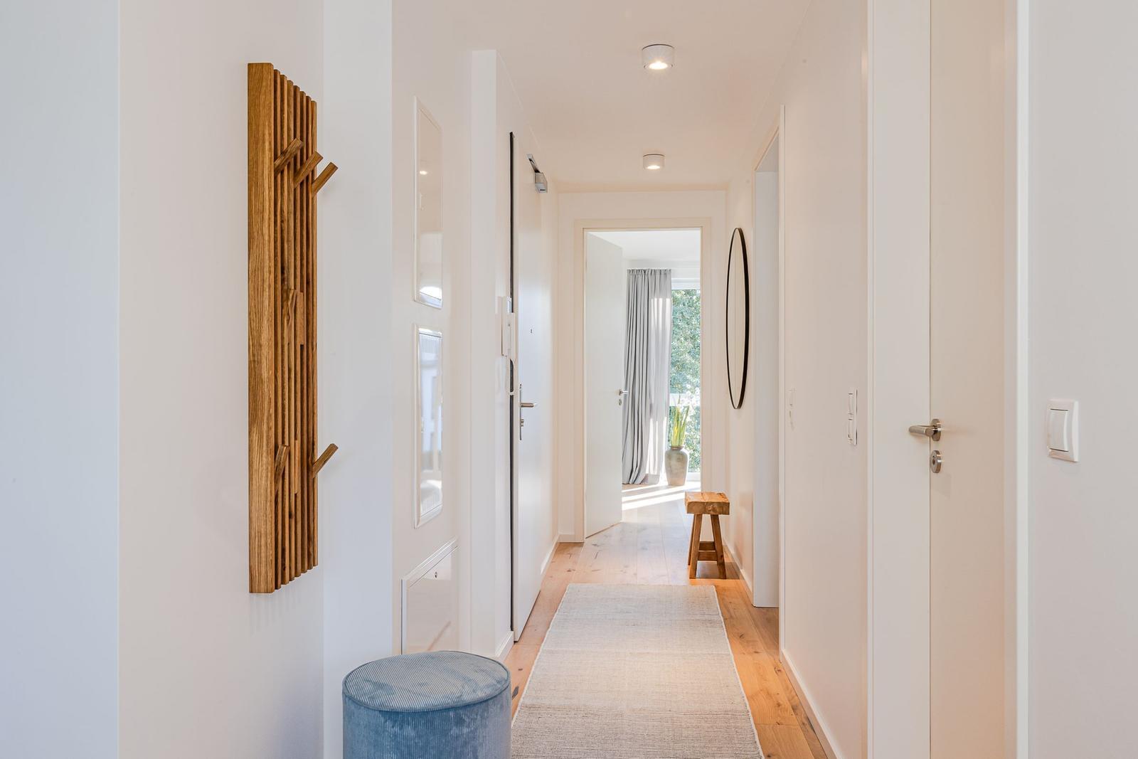 Flur mit Holzboden, Wandgarderobe und Blick in Wohnbereich.