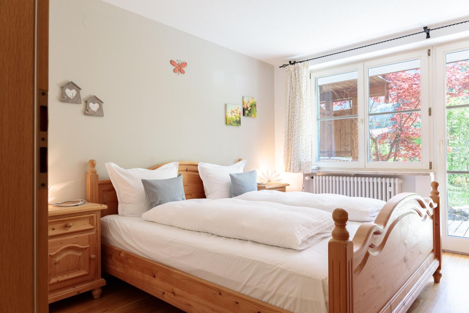 Bedroom with wooden bed, nightstand, and window with view of trees.