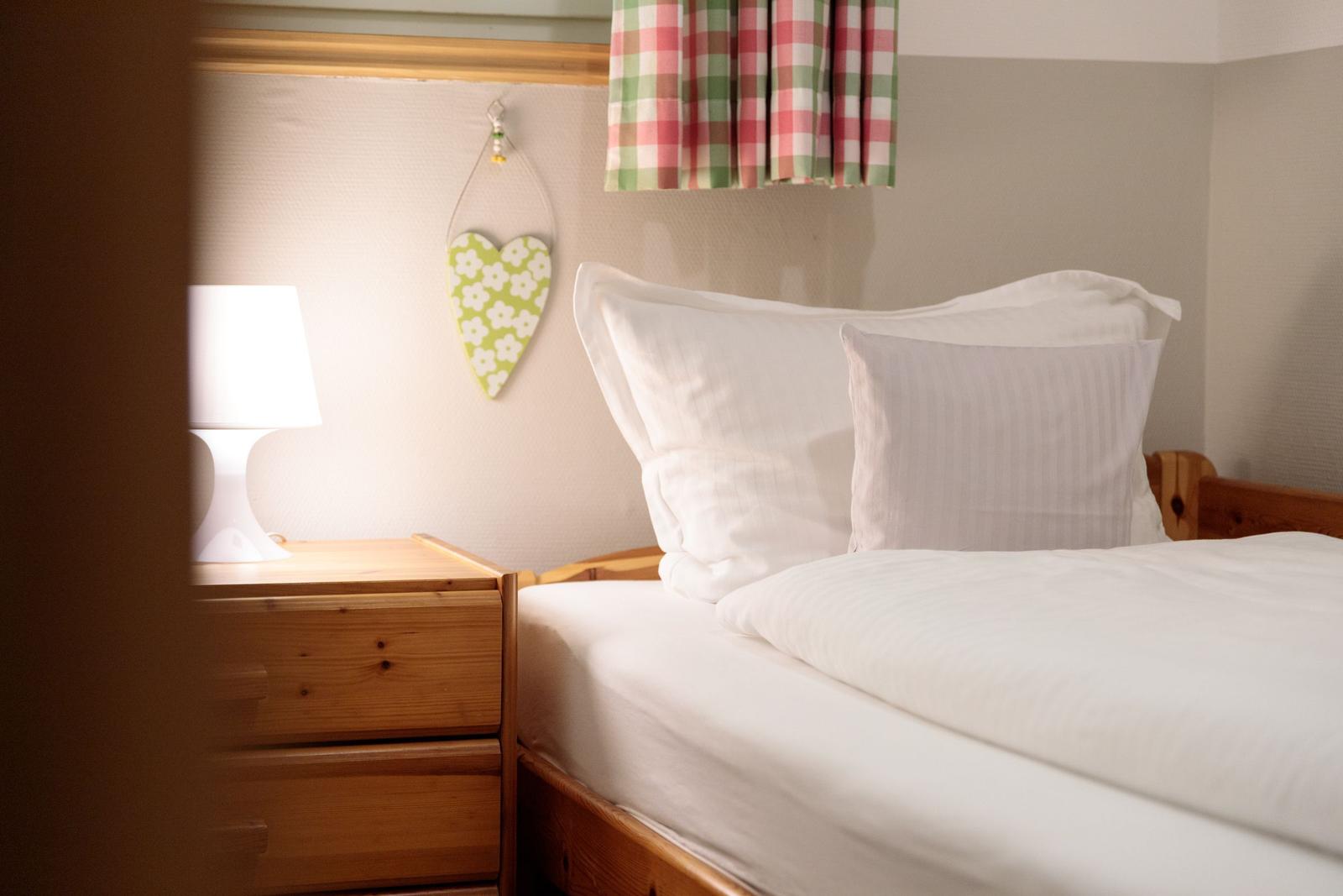 A bed with white pillows and bedding, next to a nightstand with lamp and heart decoration.