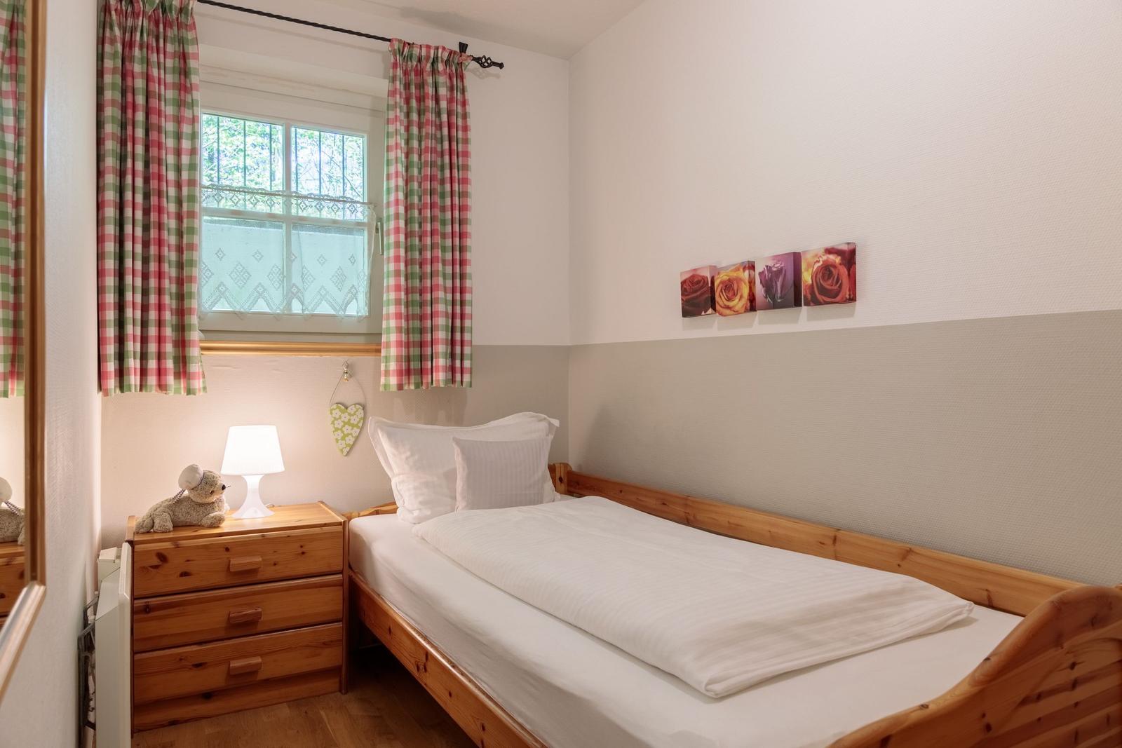 A bedroom with wooden bed, nightstand, and window with checkered curtains.
