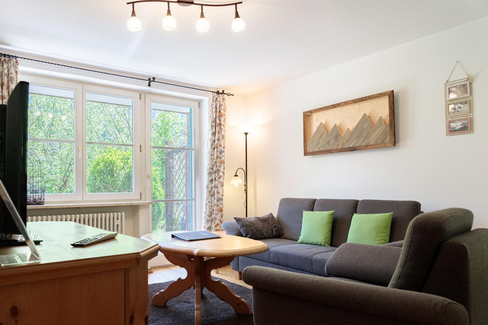 Living room with sofa, table, and window. Wall art and floor lamp are visible.