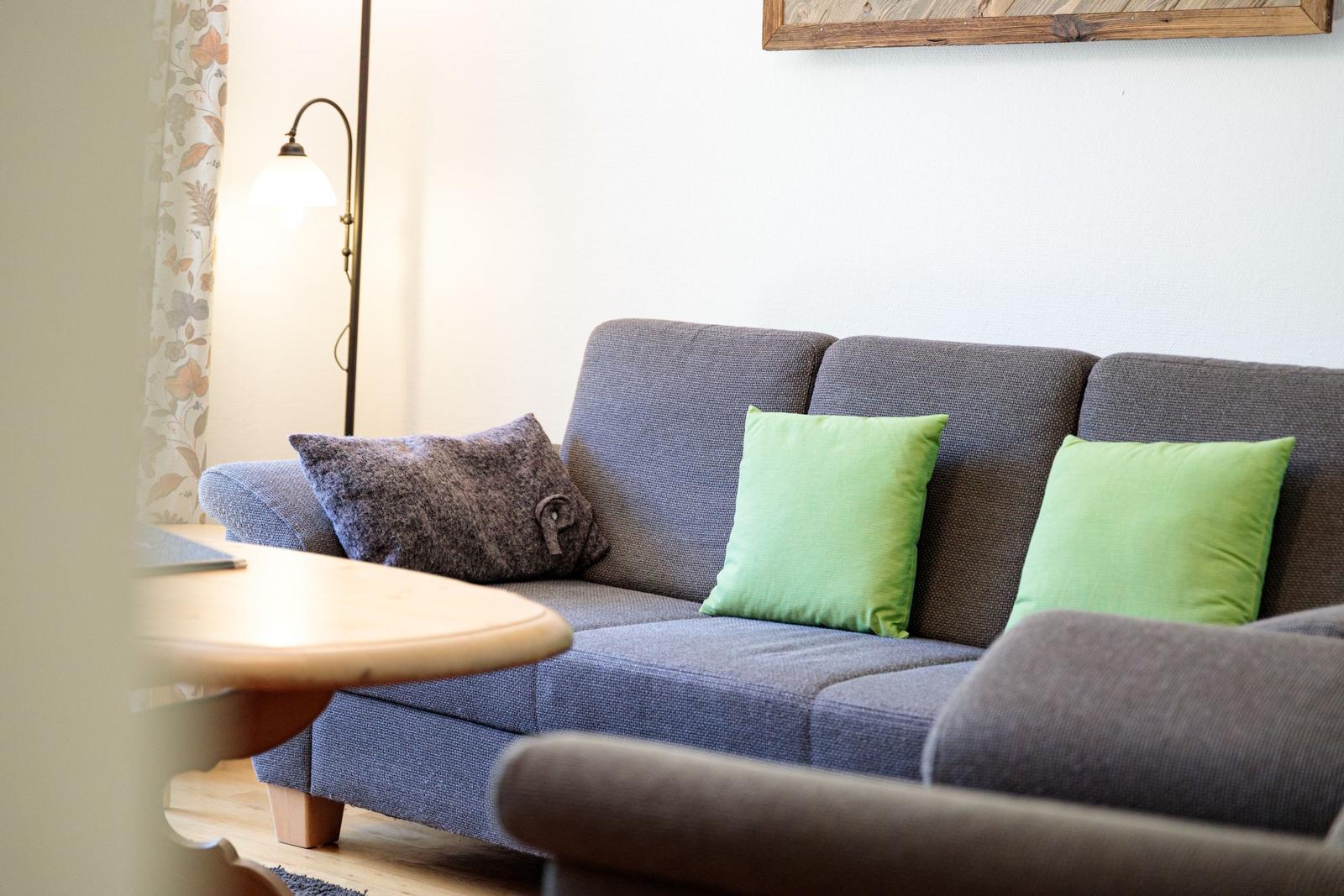 A gray sofa with two green and one dark cushion.