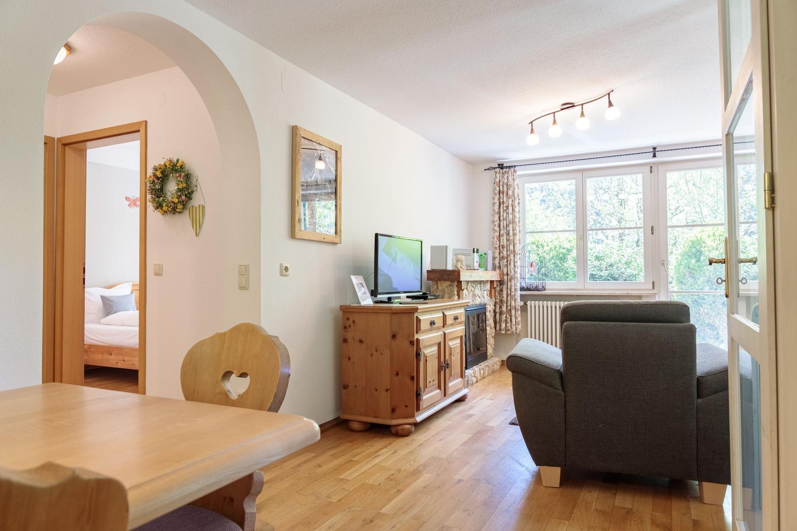 Living area with seating, TV, and wooden table. Passage to bedroom.