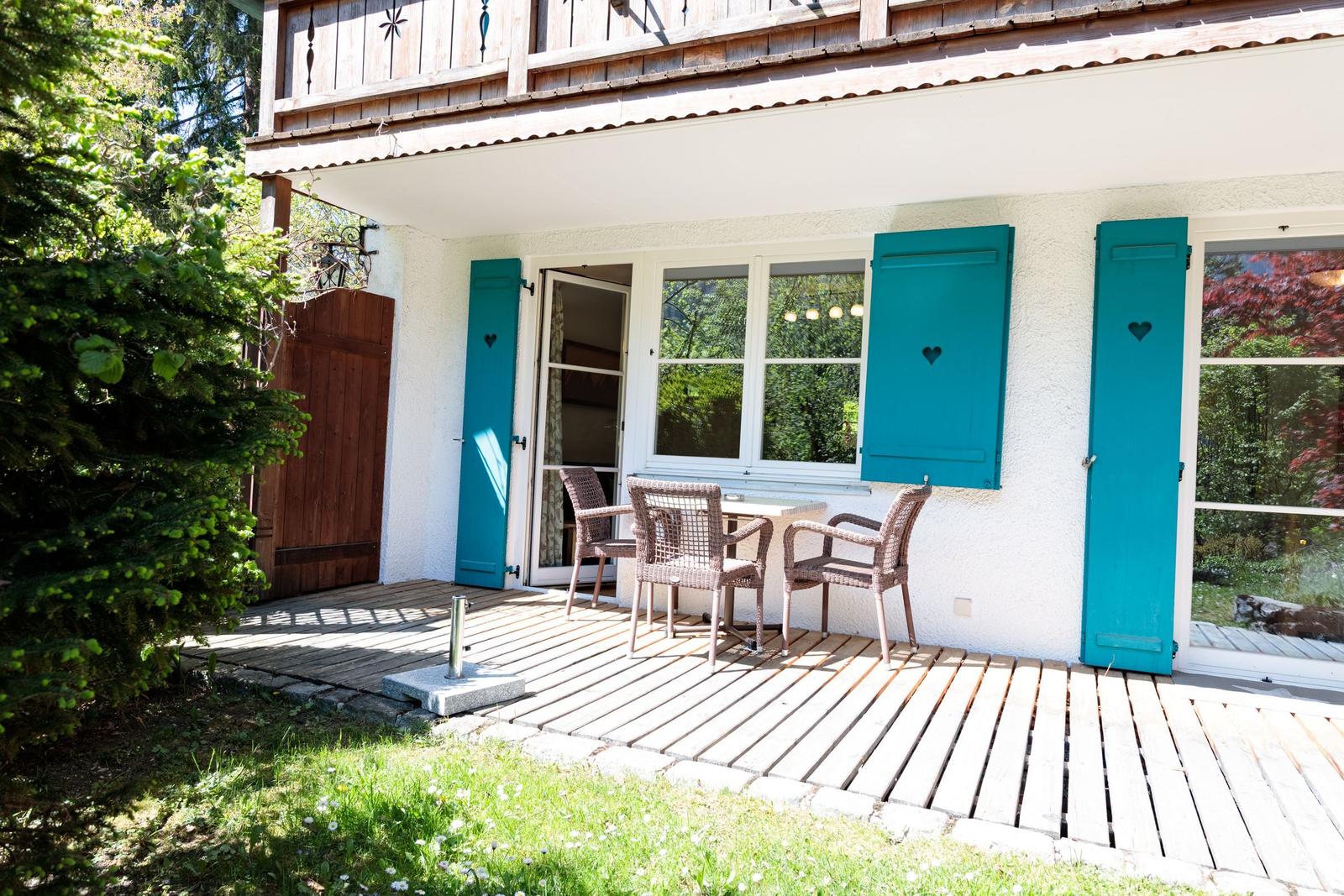 Deck with table and chairs, blue shutters, and wooden veranda.
