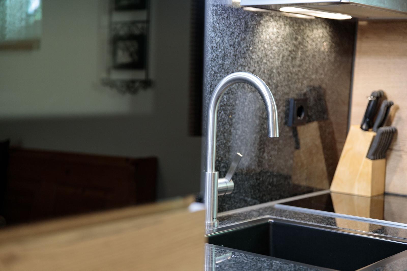 Kitchen faucet with water spray, dark countertop, and knife block in background.
