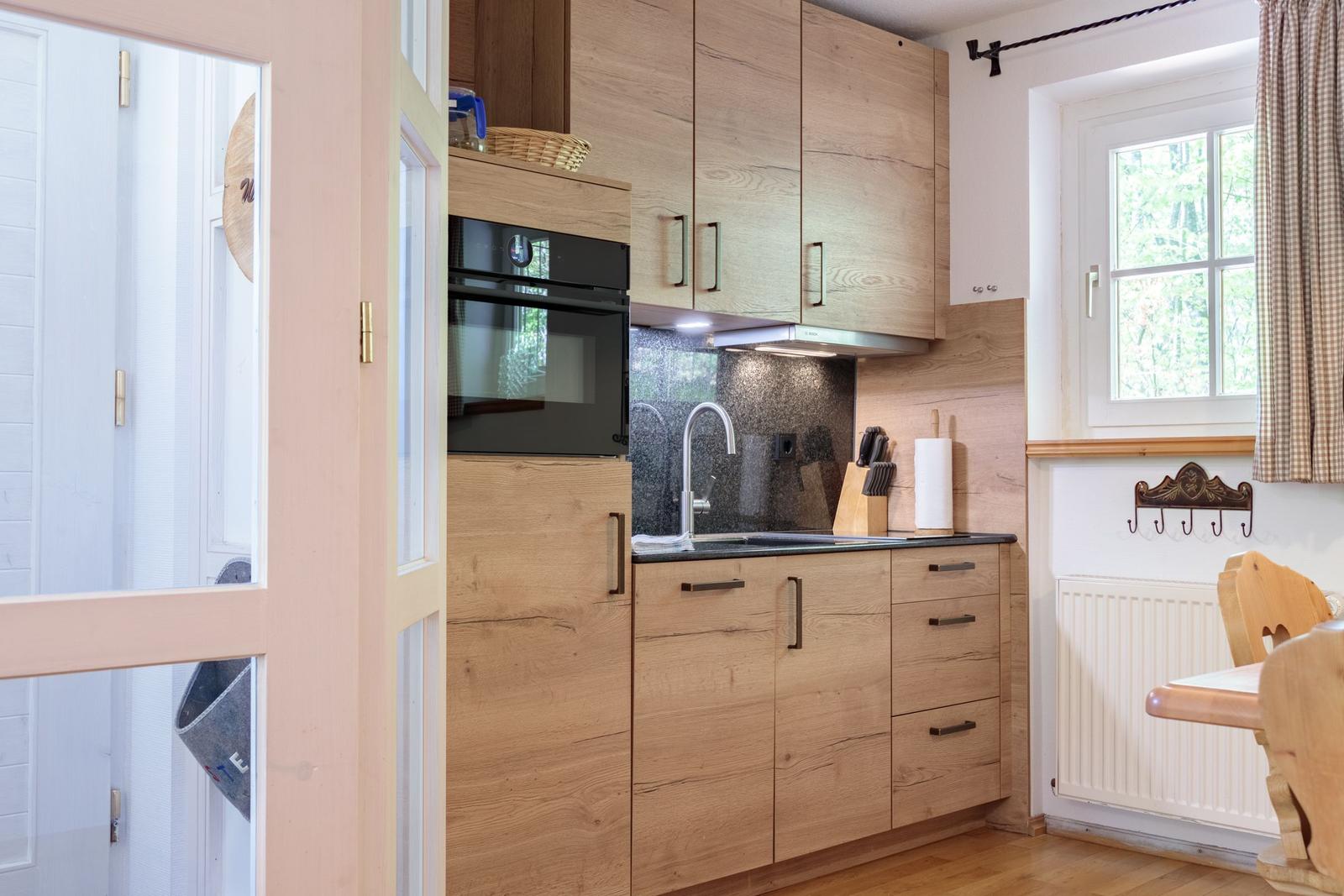 Kitchen with wooden cabinets, stainless steel sink, and window to the forest.
