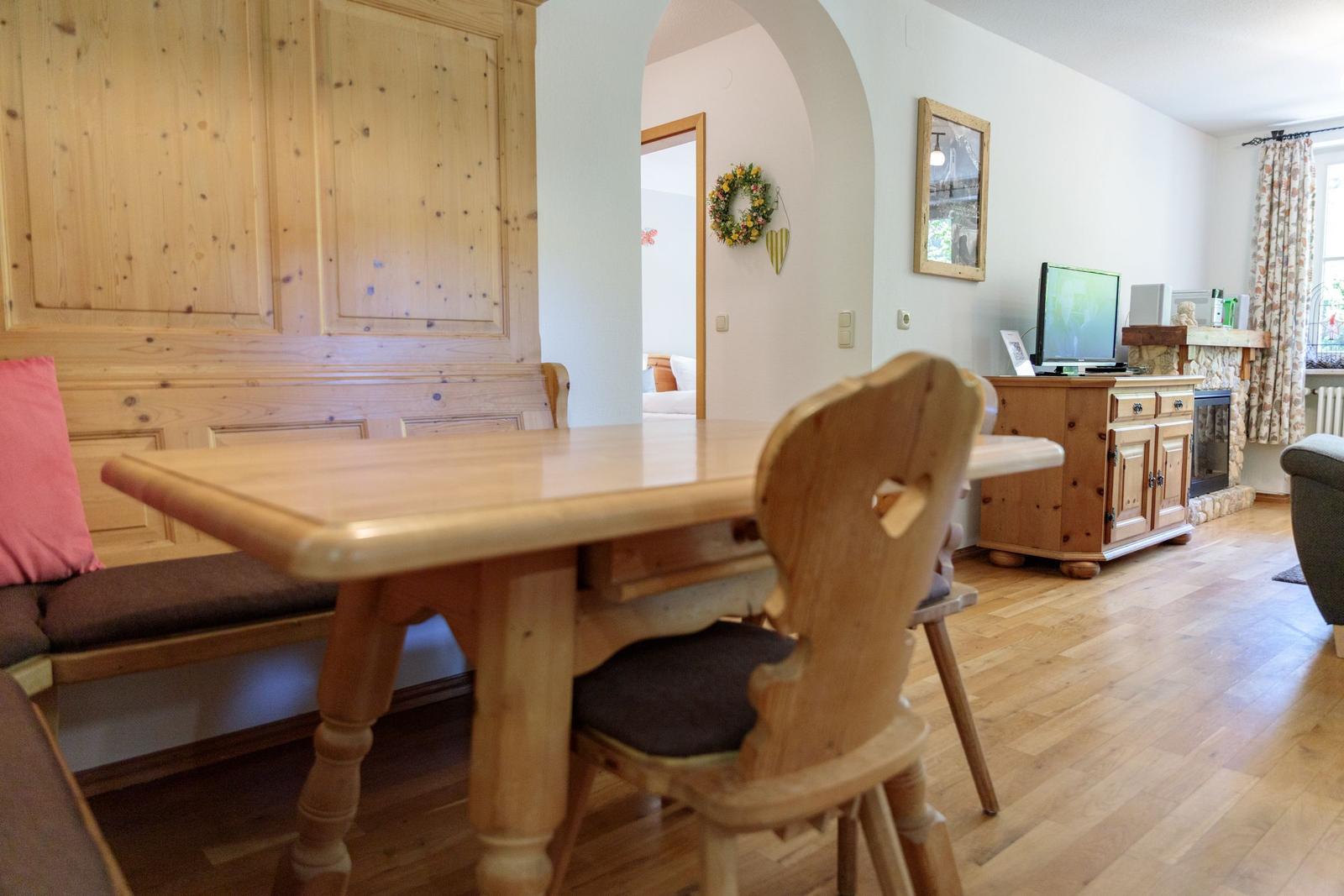 Dining area with wooden table and benches. Living room with TV and fireplace.