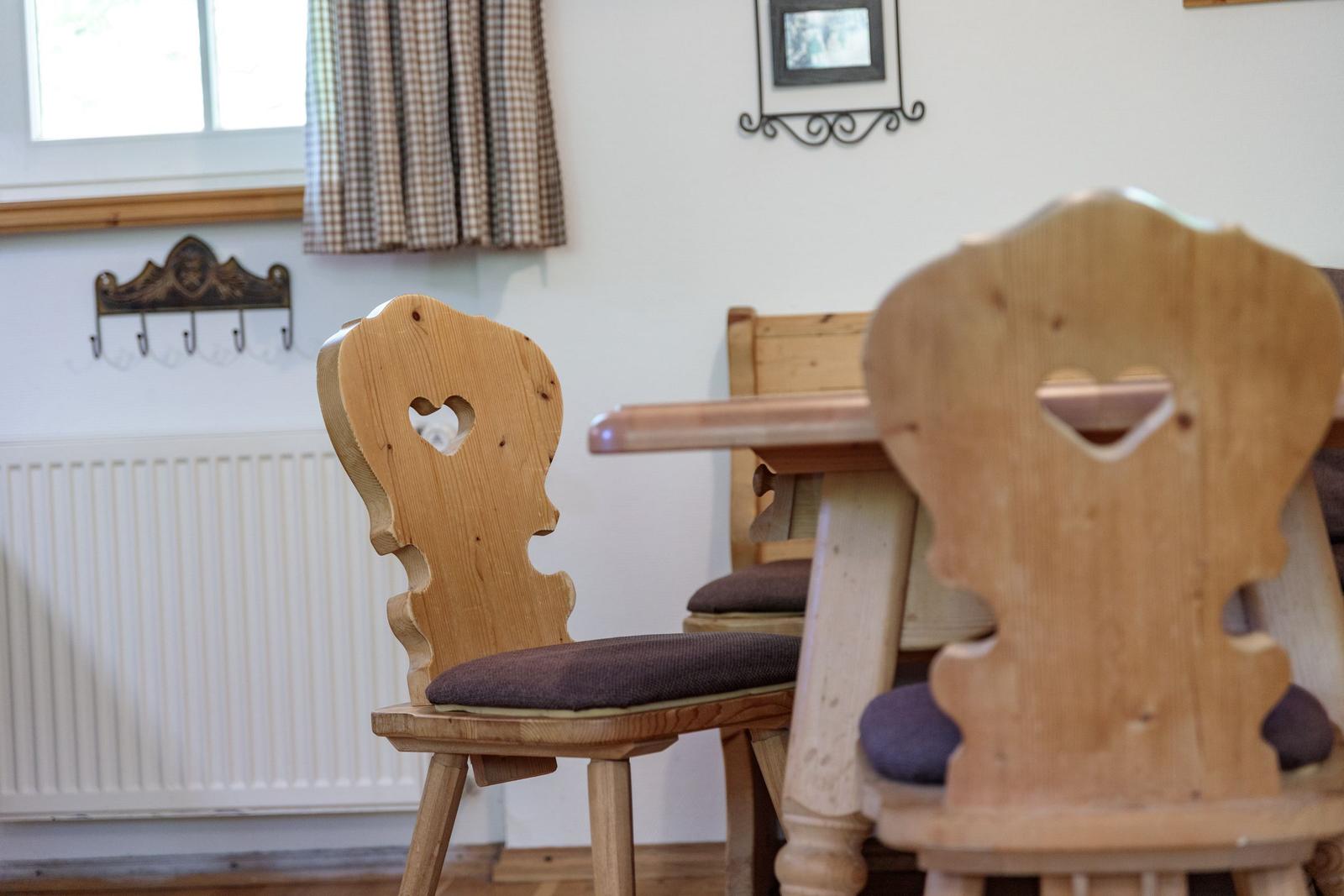 Wooden chairs with heart shape at table, wall heater and window with curtain.