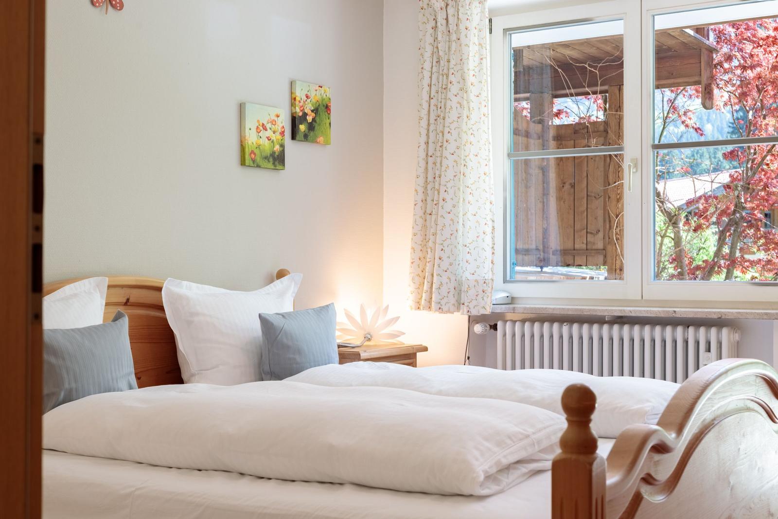 A bedroom with bed, wall art, and view of trees through window.