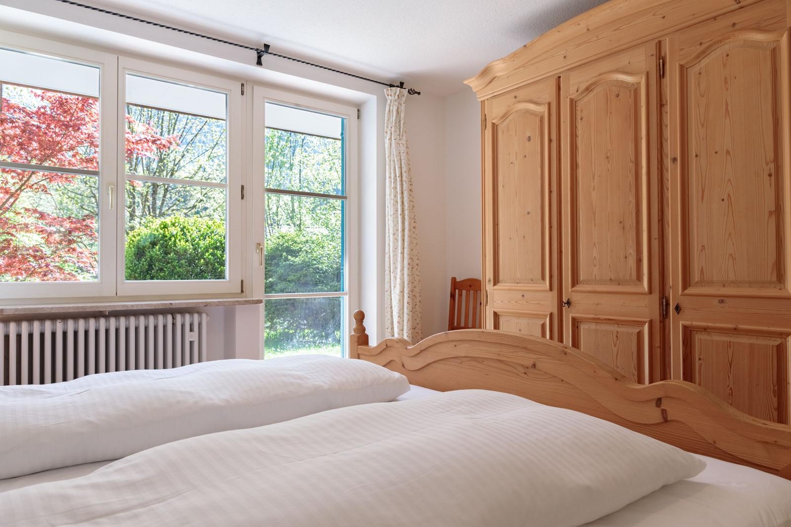 Bedroom with wooden bed, wardrobe, and window view of trees.